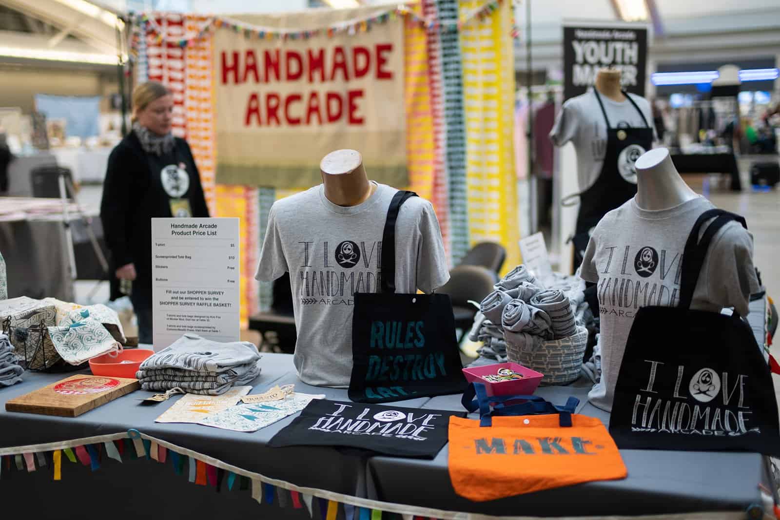 A photo of shirts, bags, and other merchandise for sale at Handmade Arcade.