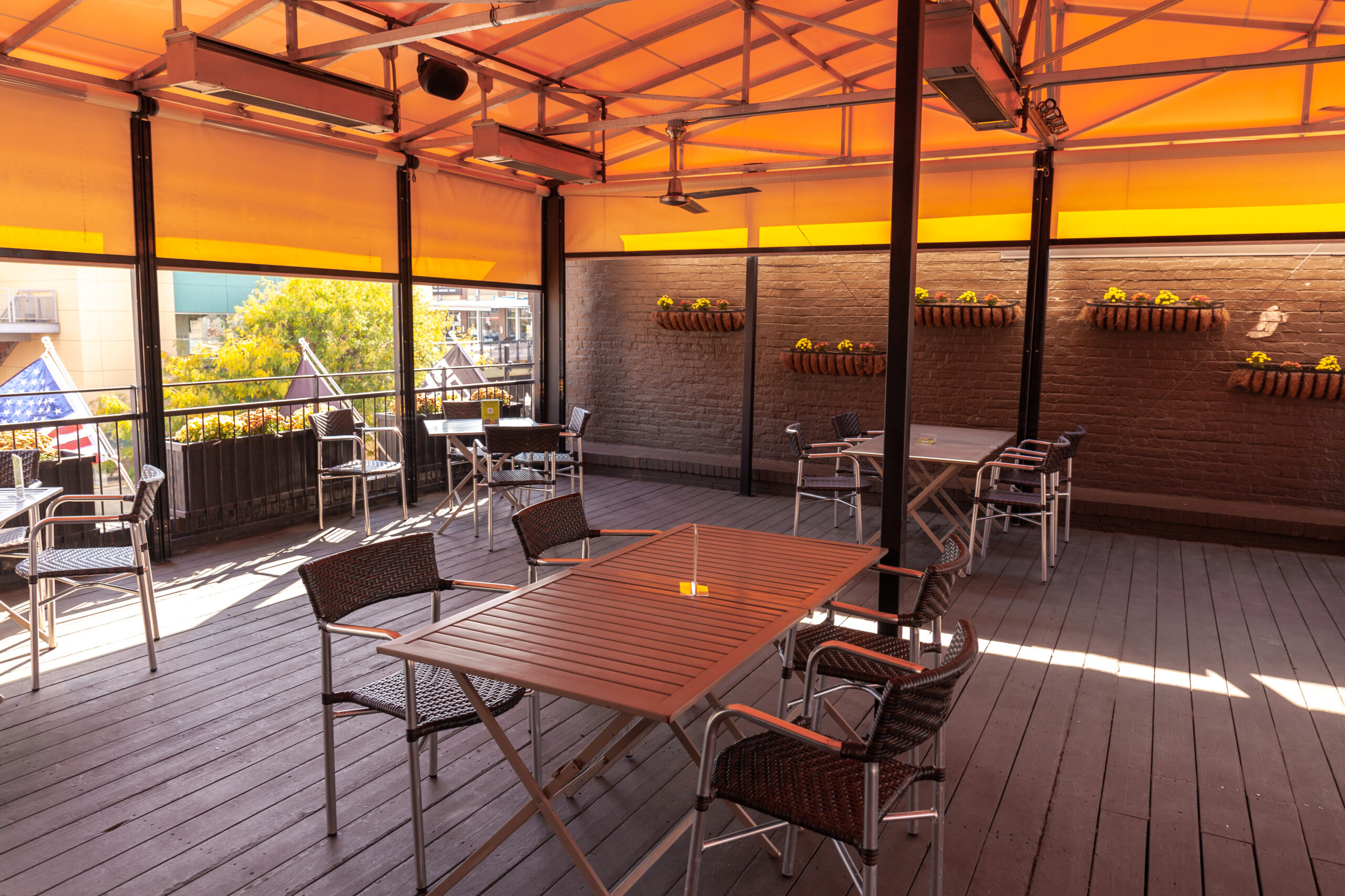 A photo of the outdoor dining area at Square Cafe. There is an orange awning and warm colored flowers for a cozy outdoor vibe.