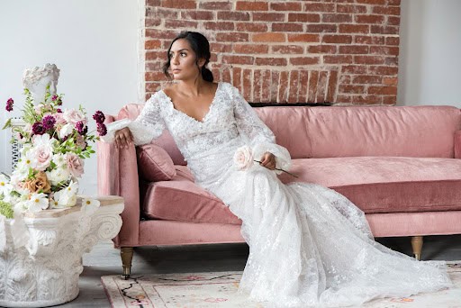 A photo of a bride posing on a couch in a long sleeve dress.