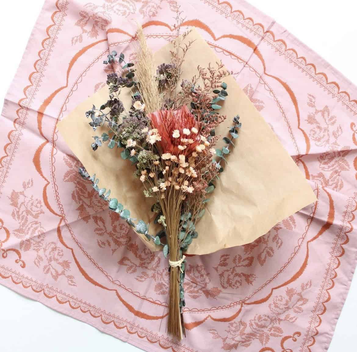 A photo of a delicate dried flower bouquet laying on a pink flowery bandana.