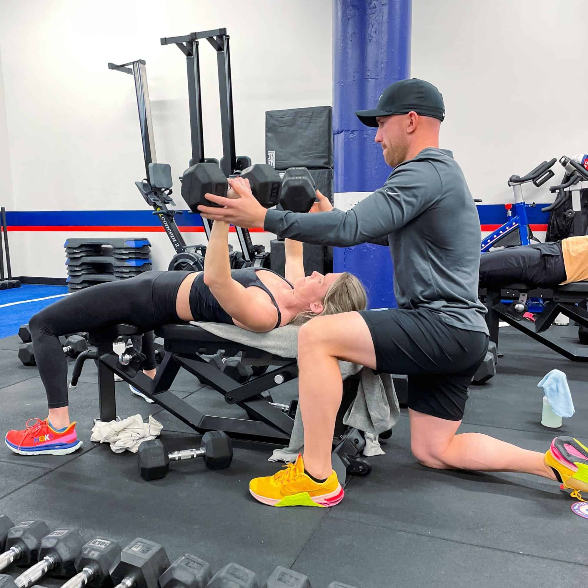 A photo of a trainer and someone working out with weights.
