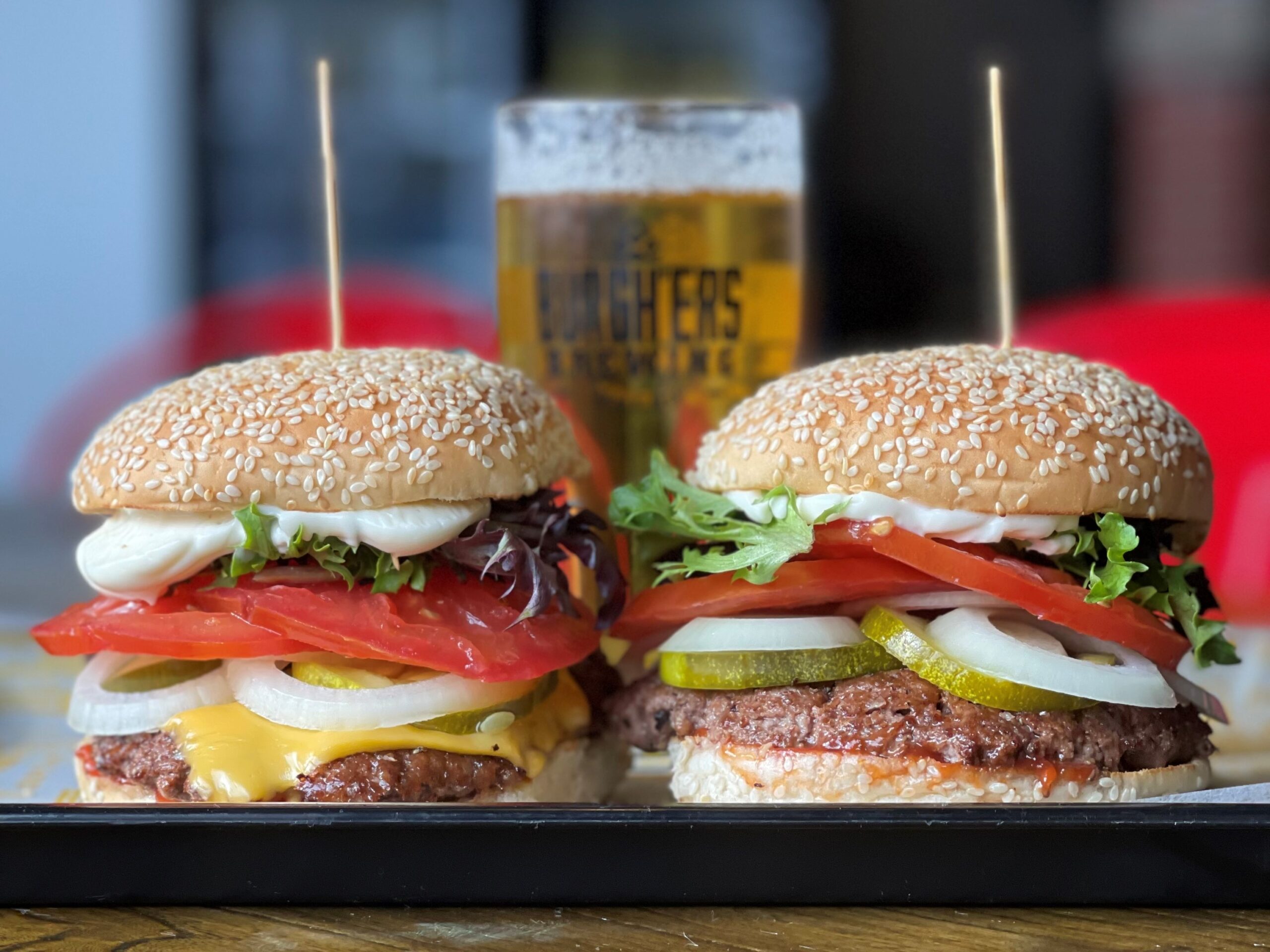 A photo of two burgers at Burghers with a beer in the background.