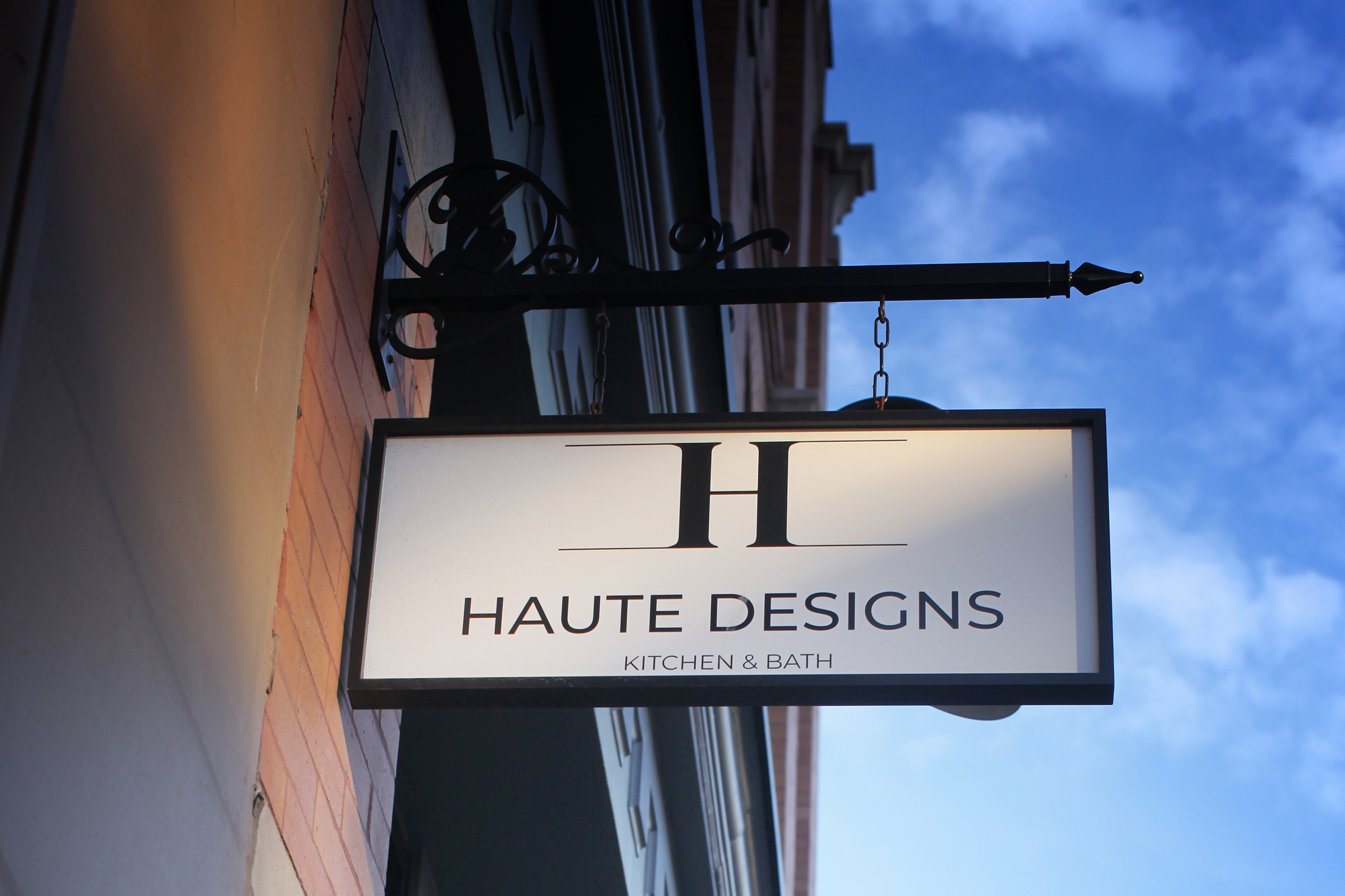 A photo of the sign outside at Haute Designs. It has an "H" designed logo, reading "Haute Designs / Kitchen & Bath" underneath.