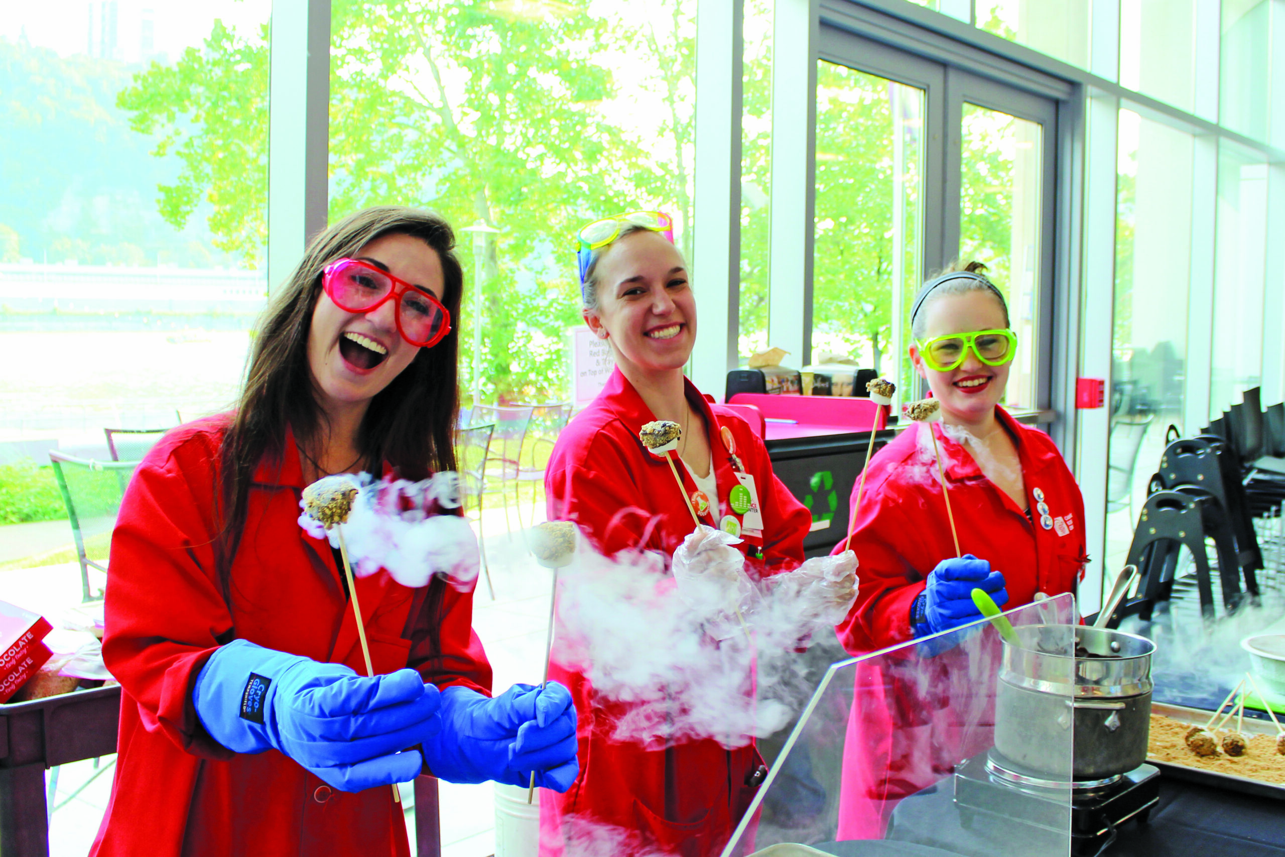 Three people in red lab coats serving cake pops at the Carnegie Science Center.