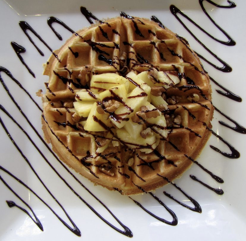 A photo of a sweet waffle topped with fruit, nuts, and a chocolate drizzle from Waffles, INCaffeinated.