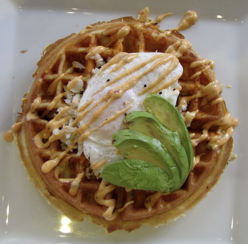 A photo of a savory waffle topped with avocado from Waffles, INCaffeinated.