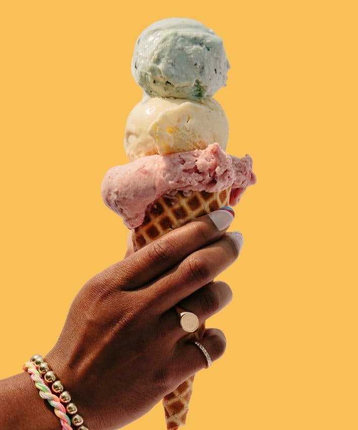A photo of a person holding an ice cream cone with 3 scoops.
