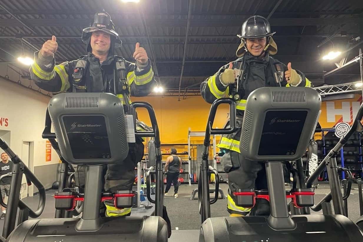 Two men in full turnout firefighting gear use the StairMaster machines at Crunch Fitness to complete the 9/11 Remembrance Stair Climb challenge.