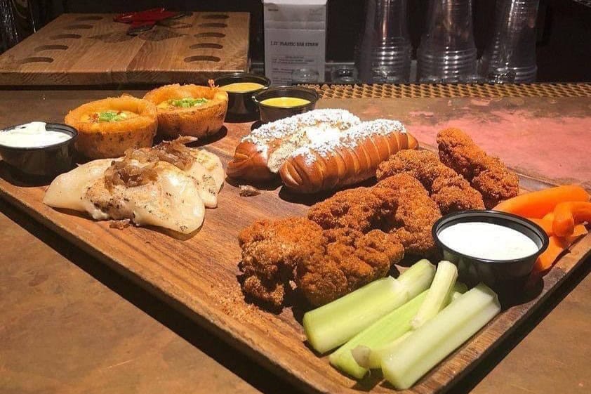 A photo of pierogis, fresh pretzels, half chicken, carrots, and celery on a wooden platter.