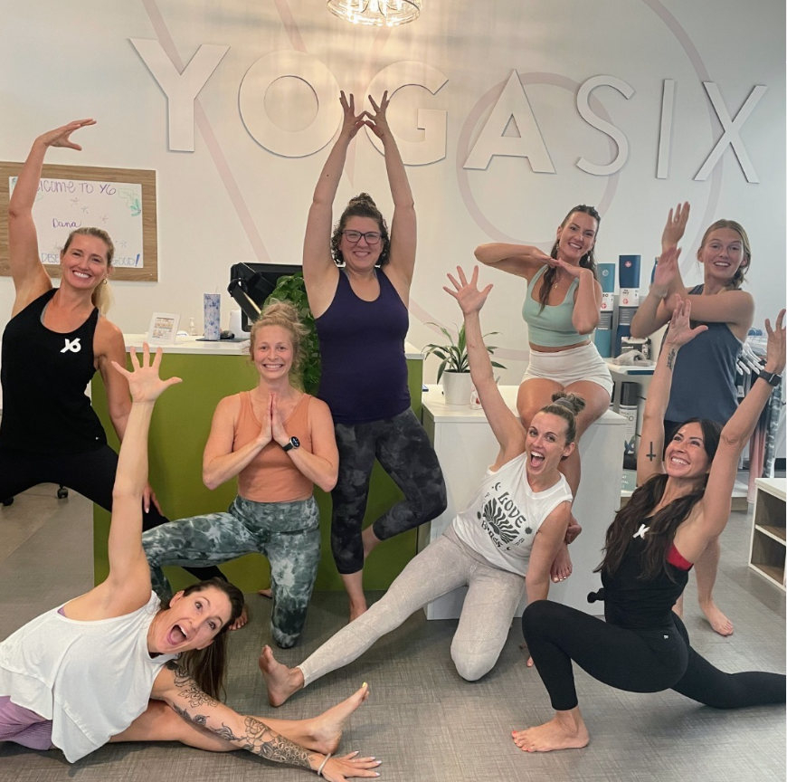 A photo of people smiling and doing yoga poses at YogaSix.