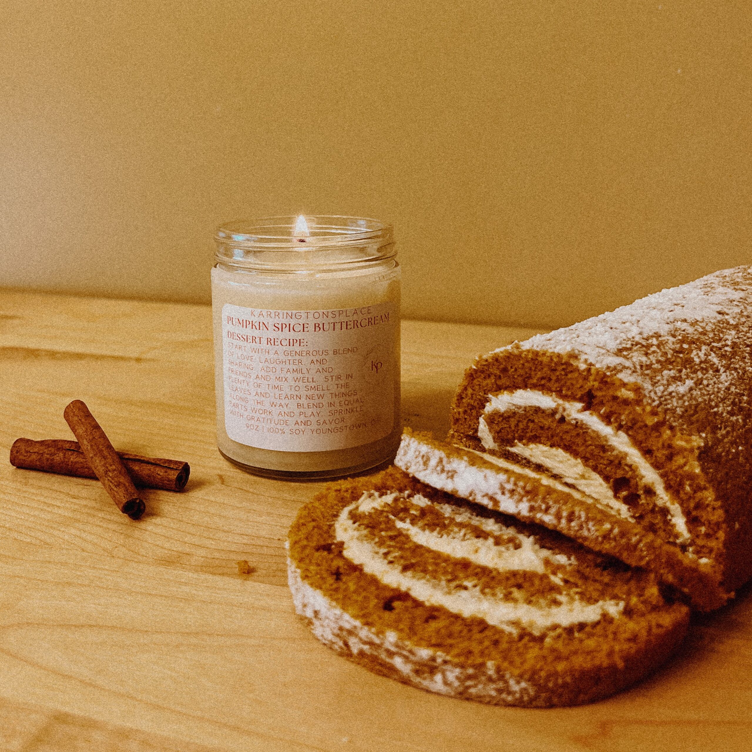 A photo of a Karrington's Place pumpkin spice buttercream candle next to pumpkin swirl bread and cinnamon sticks.