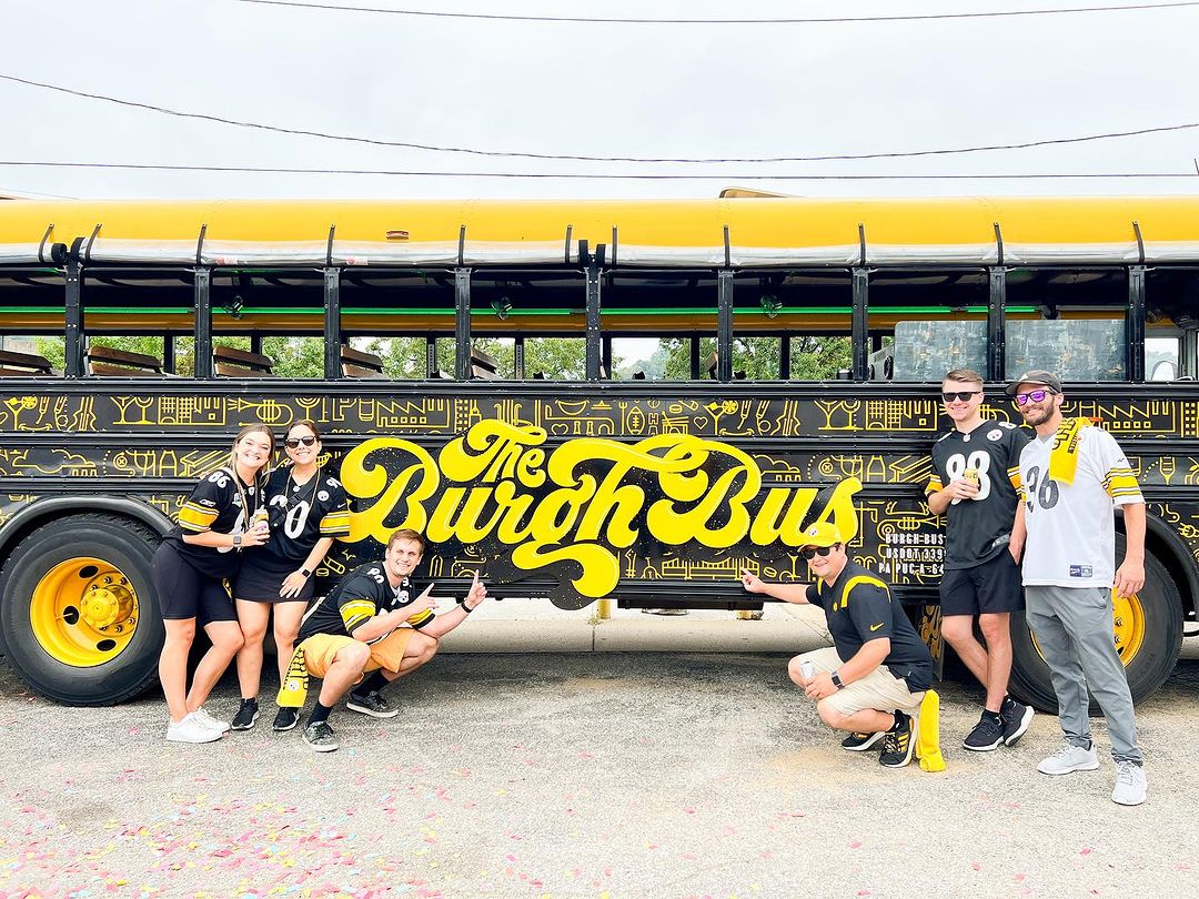 A photo of Steelers fans posing outside of the Burgh Bus, which will be at the Great Yinzer Tailgate on November 4th, 2023.