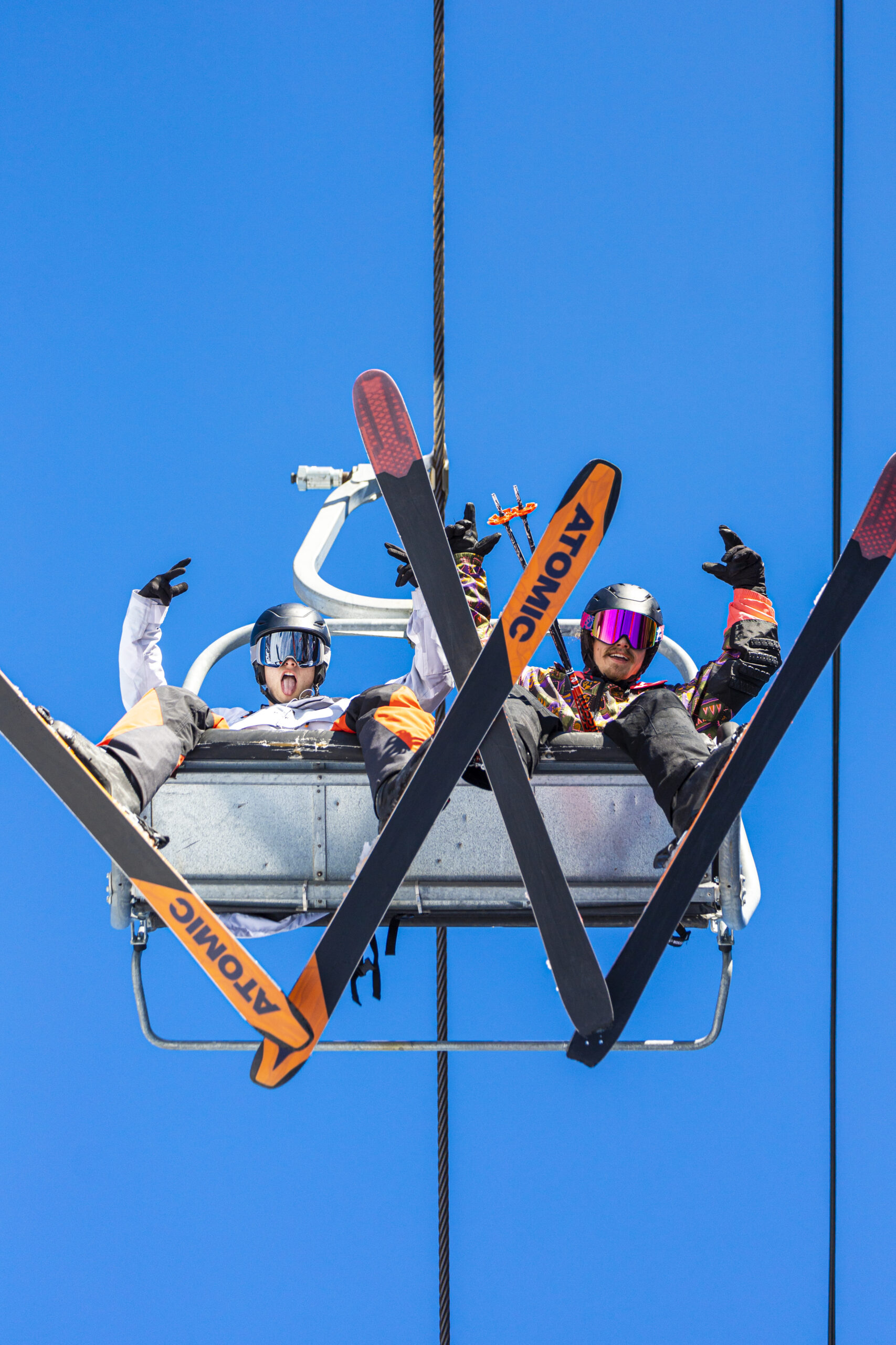 Two people posing on the ski lift with a blue sky above them.