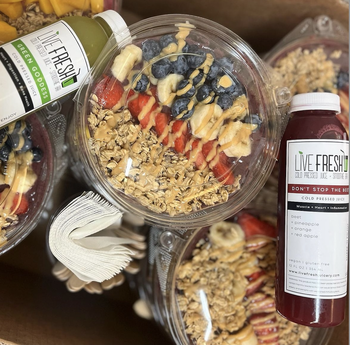 An Açaí Bowl at Live Fresh Juicery in a plastic container with bottles of juice next to it.