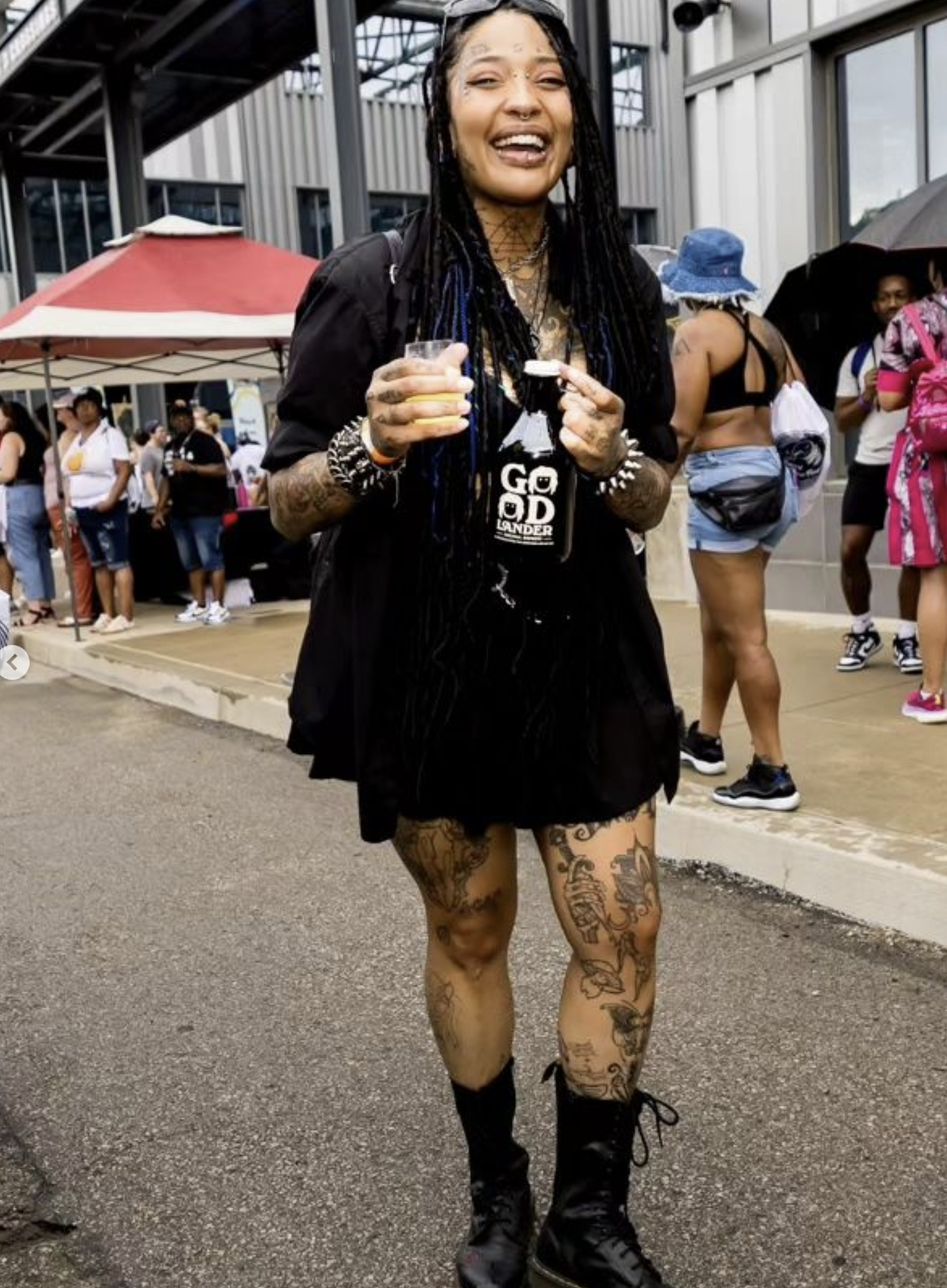 A Black person with tattoos laughing with a drink in their hands at the Barrel & Flow Festival.