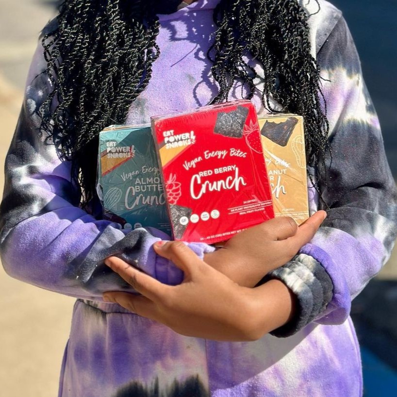 A Black person holding 3 boxes of Eat PowerSnacks in their arms.