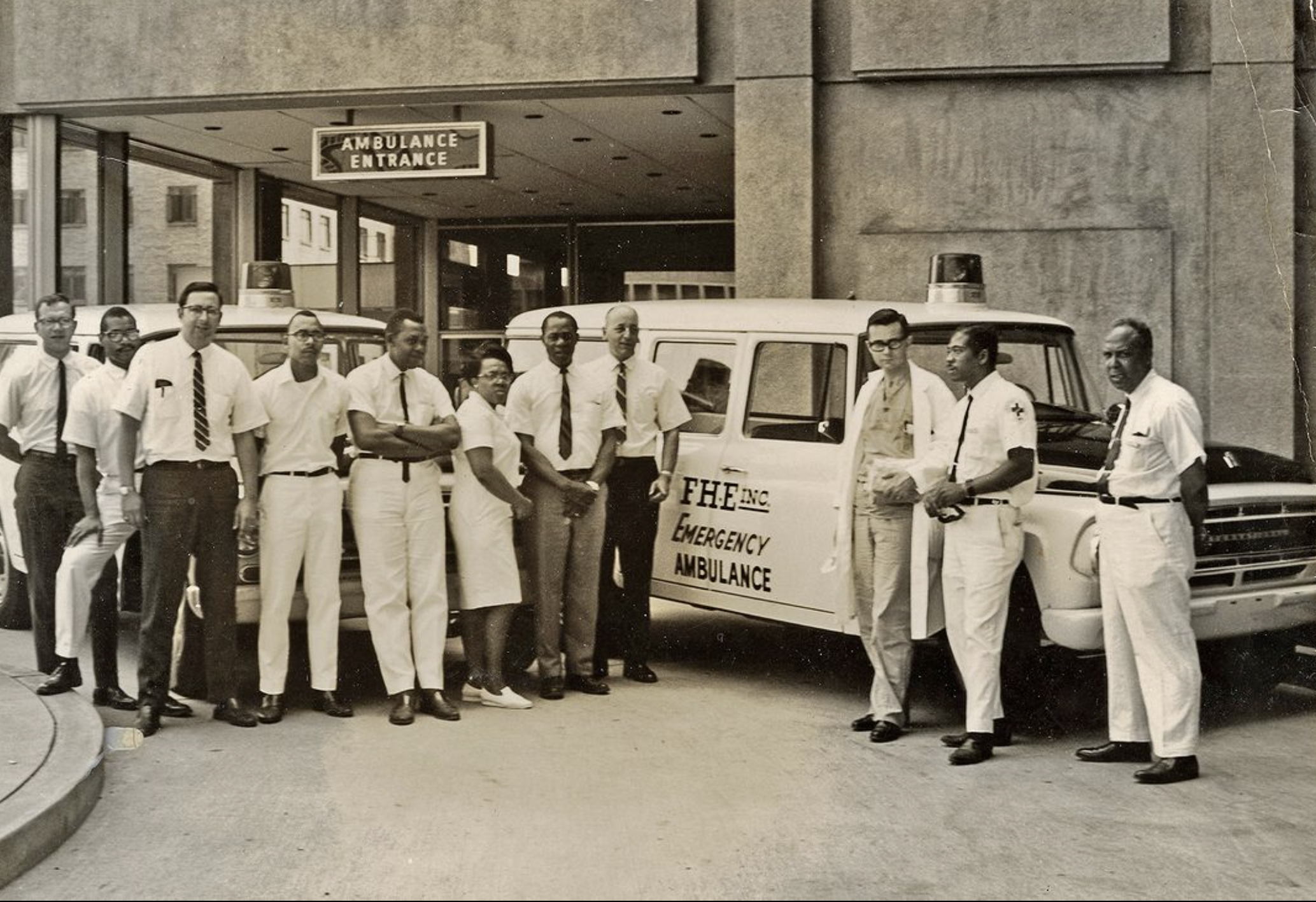 An old photo of white and Black men outside an ambulance entrance at a hospital.
