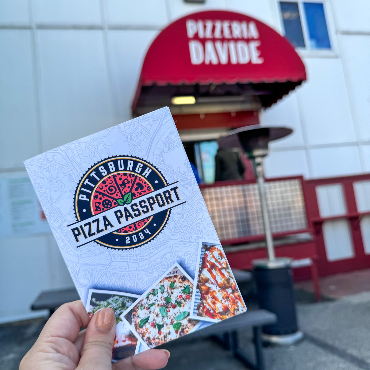 The Pittsburgh Pizza Passport book held up in front of Pizzeria Davide, one of the stops on the self-guided tour.