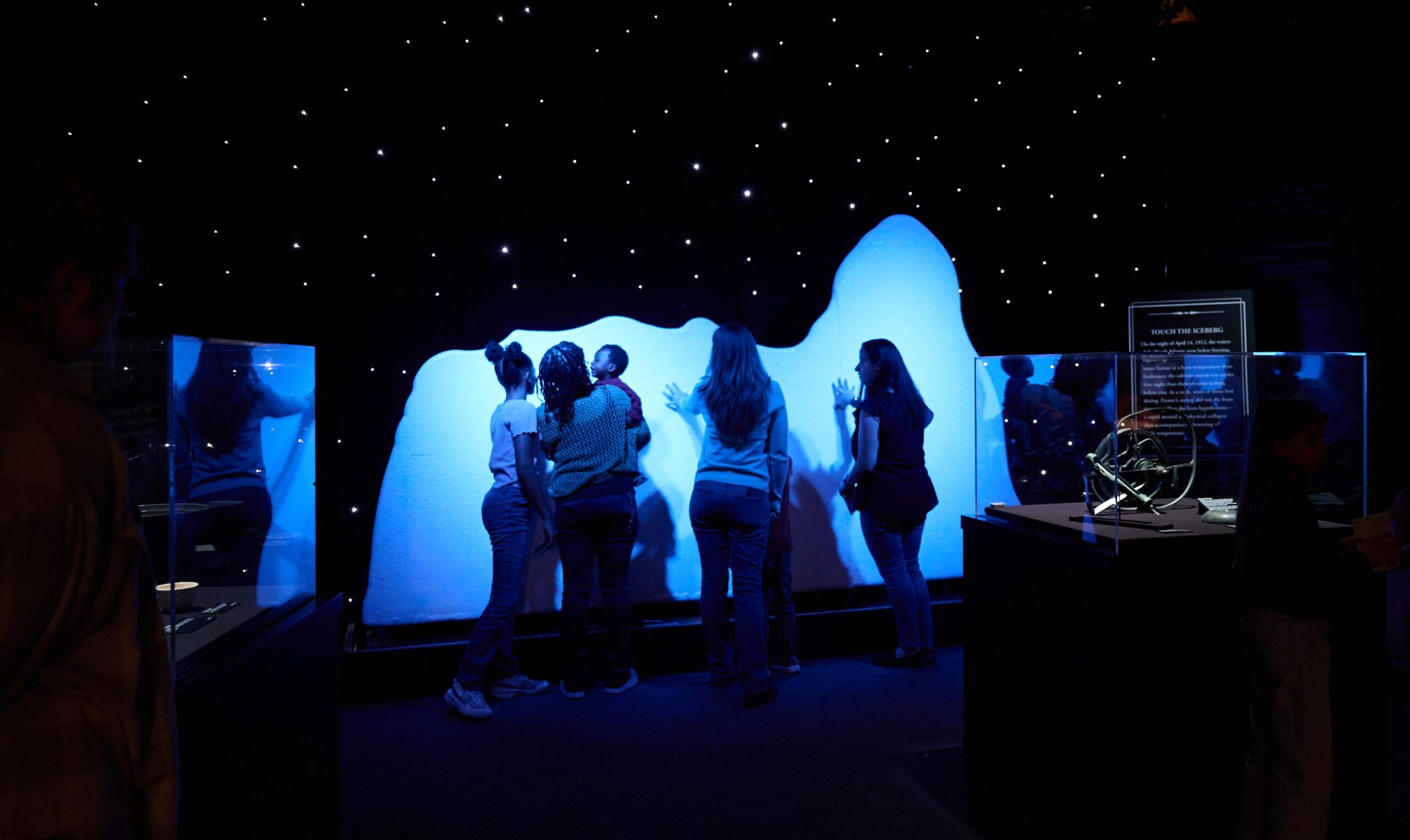 A photo of people touching the replica iceberg, lit by blue lighting, to see how cold the water and ice was on the night of the sinking.