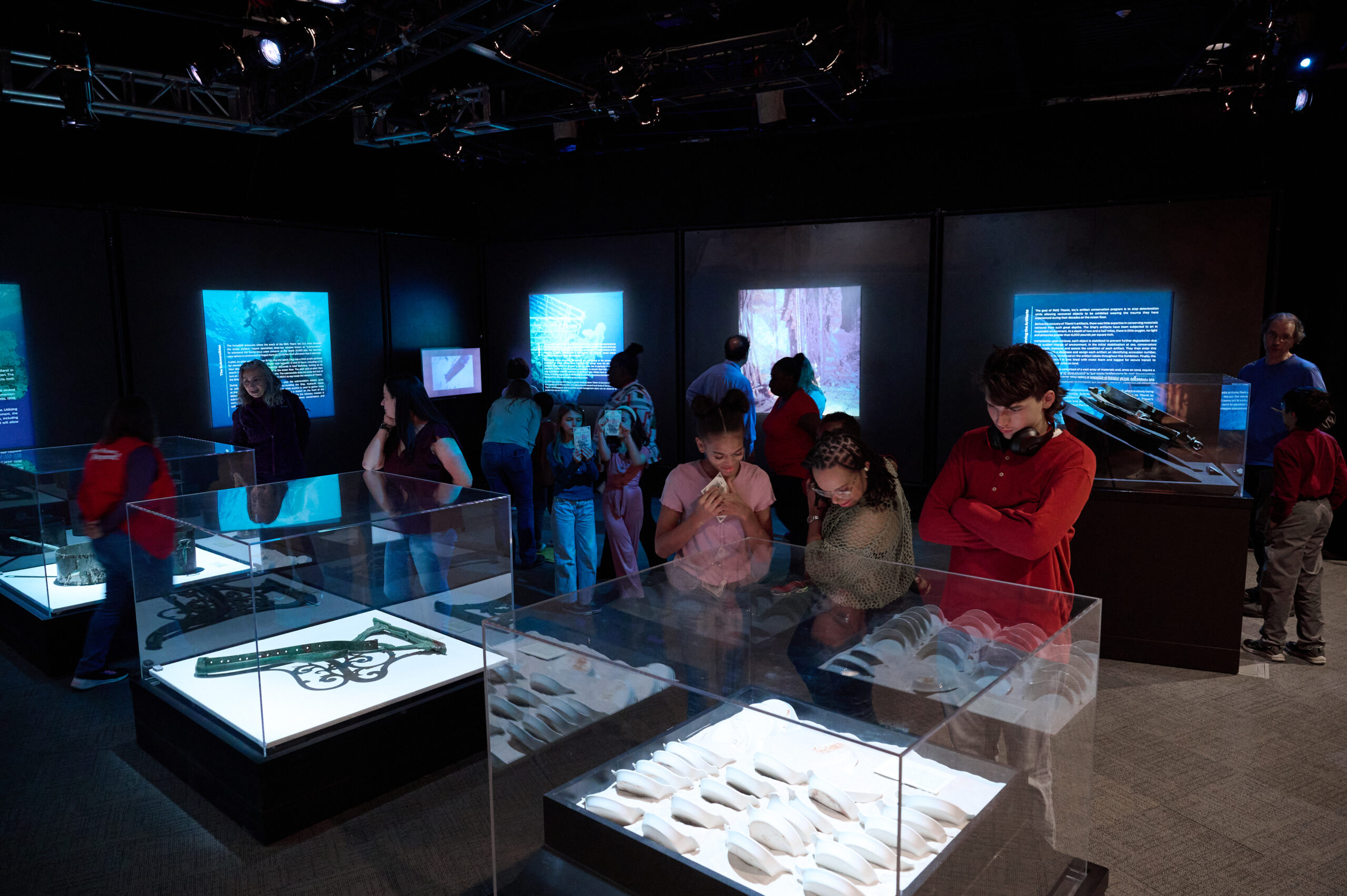 A photo of people looking at artifacts in a dark room, while others look at text and images on the walls.