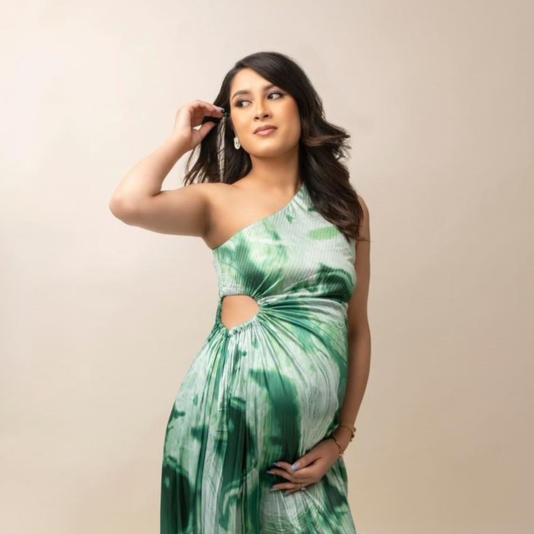 A woman posing in a white and green dress for a maternity shoot. 