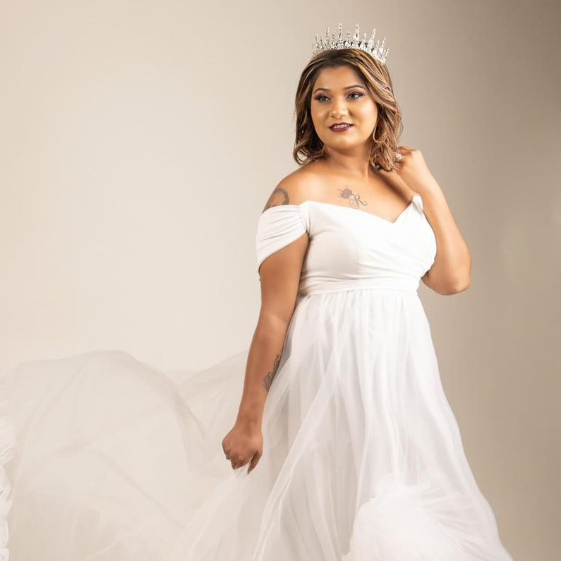 A photo of a woman posing in a white gown with a silver tiara/crown.