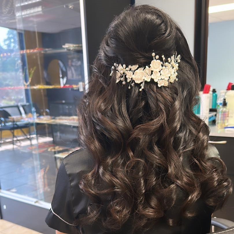 A photo of dark brown hair curled and in a half-up half-down look with a white flower accent, likely for a wedding.