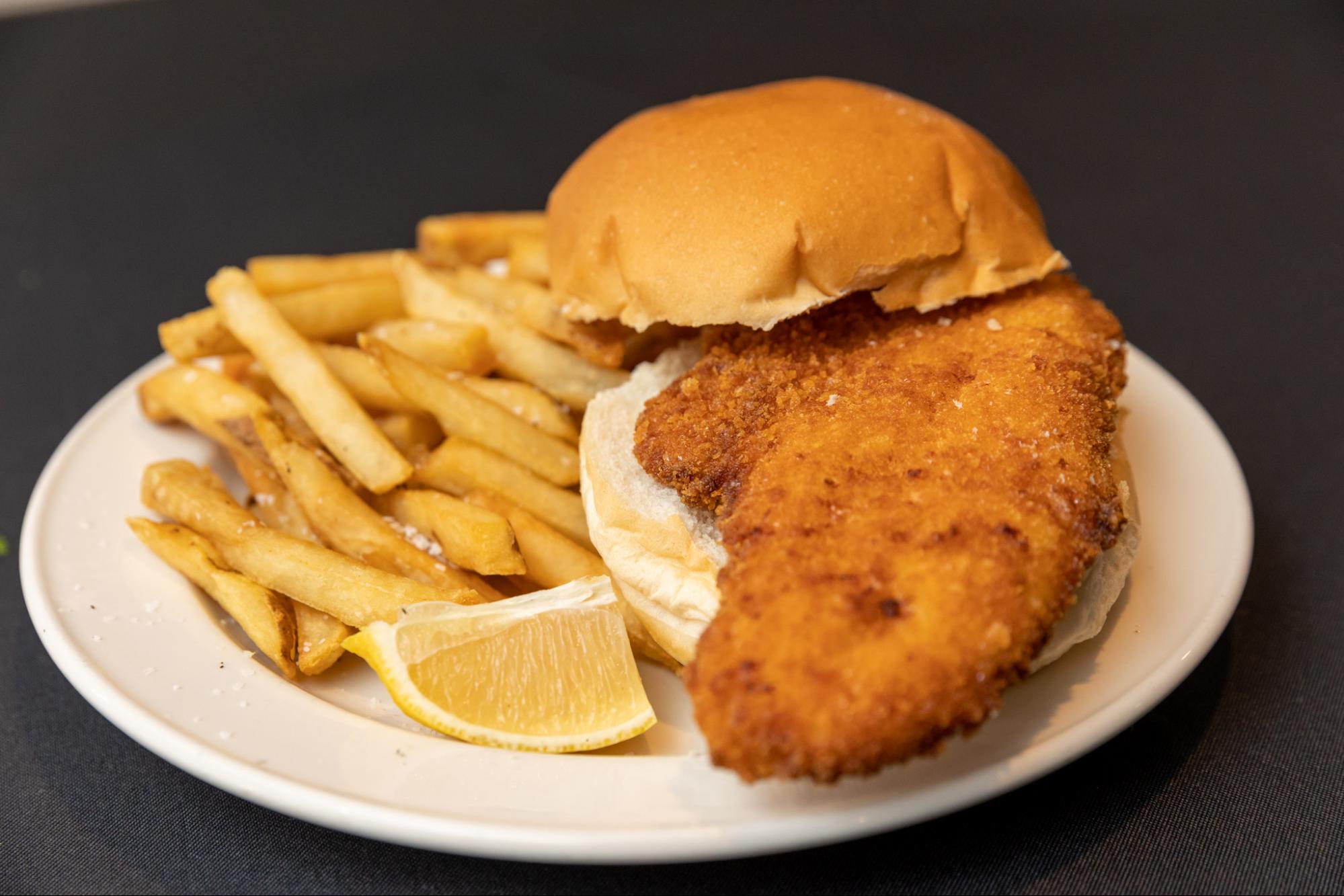 A photo of a fish sandwich from Remo's Catering with fries and a lemon on the side.