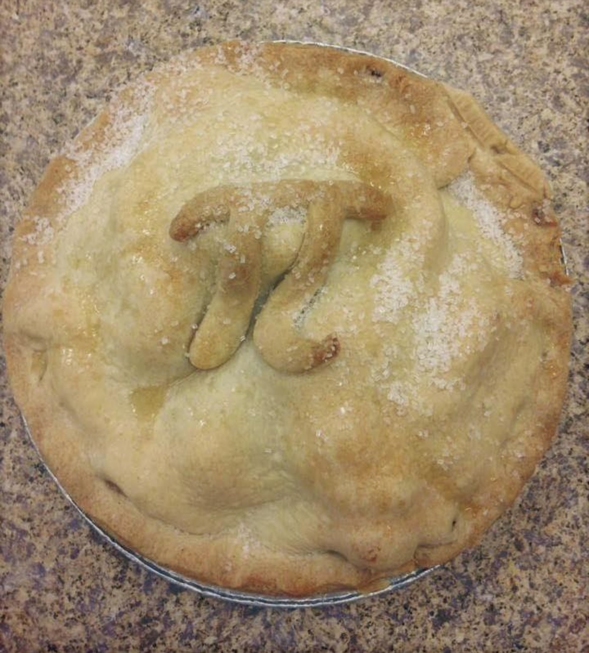 A photo of the top of a pie from the Pie Place with sugar sprinkled on top. There is a Pi symbol baked into the pie.
