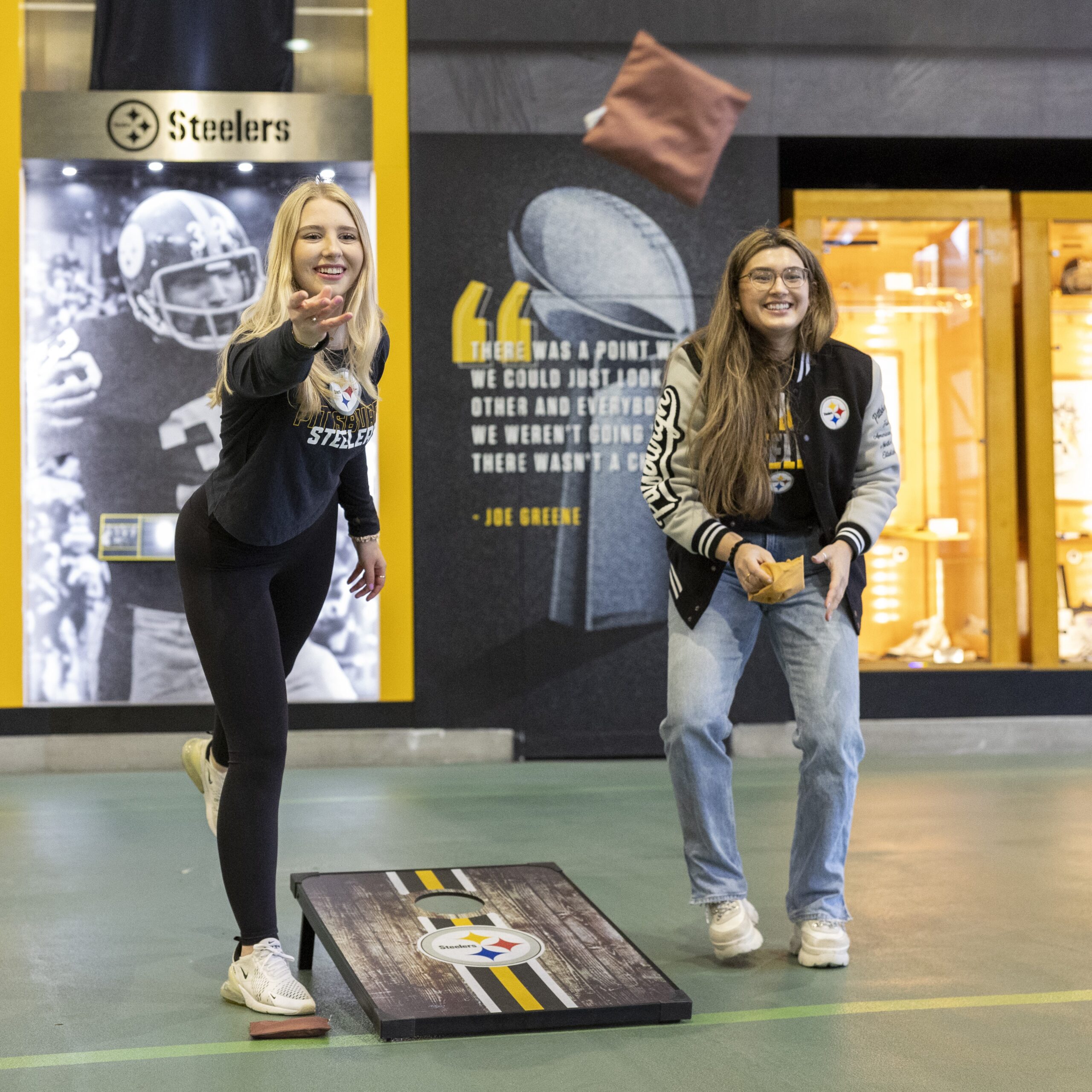 A photo of two women playing cornhole in the FedEx Great Hall at Acrisure Stadium during the SteelHERS Social.