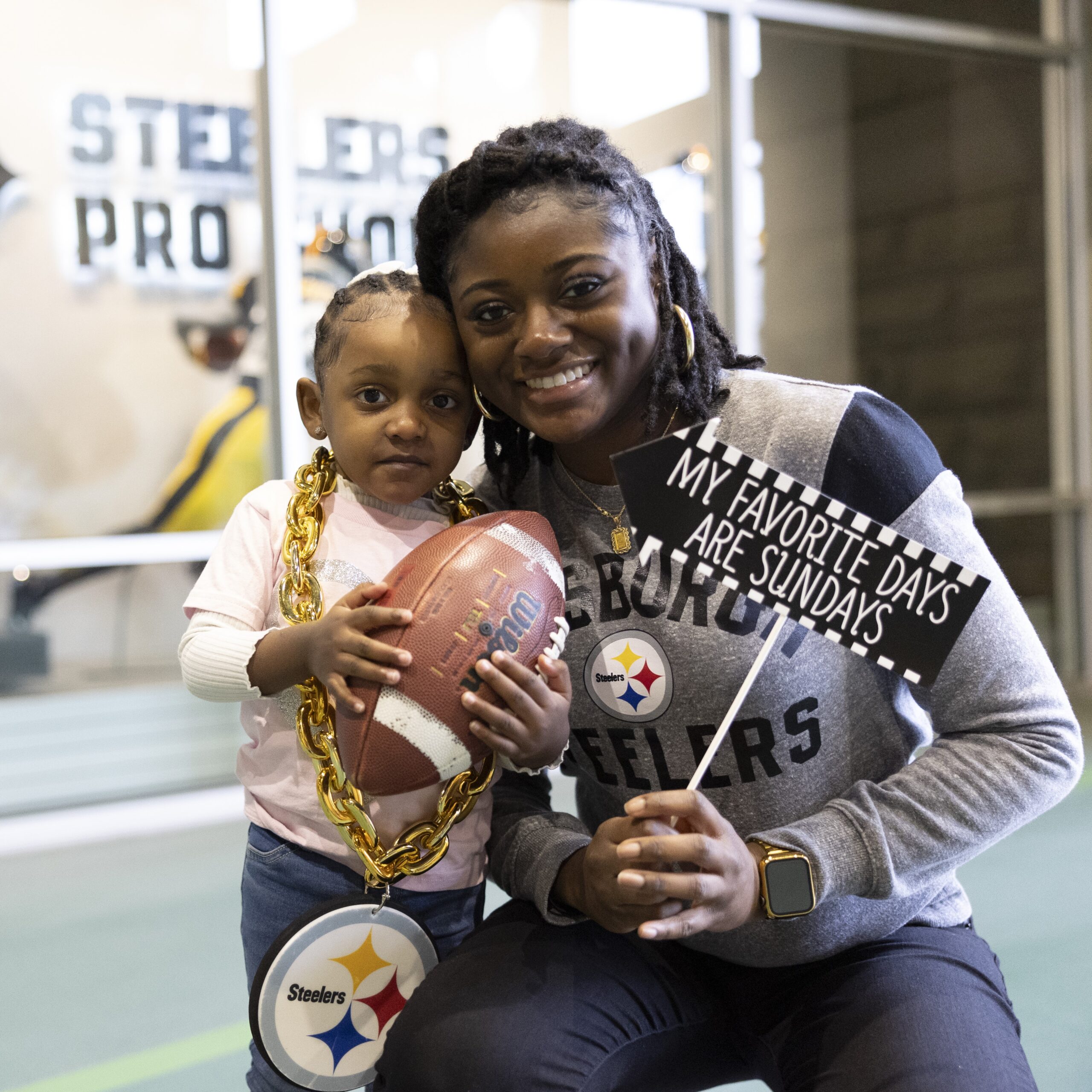 A photo of a woman posing with her young child at the SteelHERS Social event. They are holding photo op props.