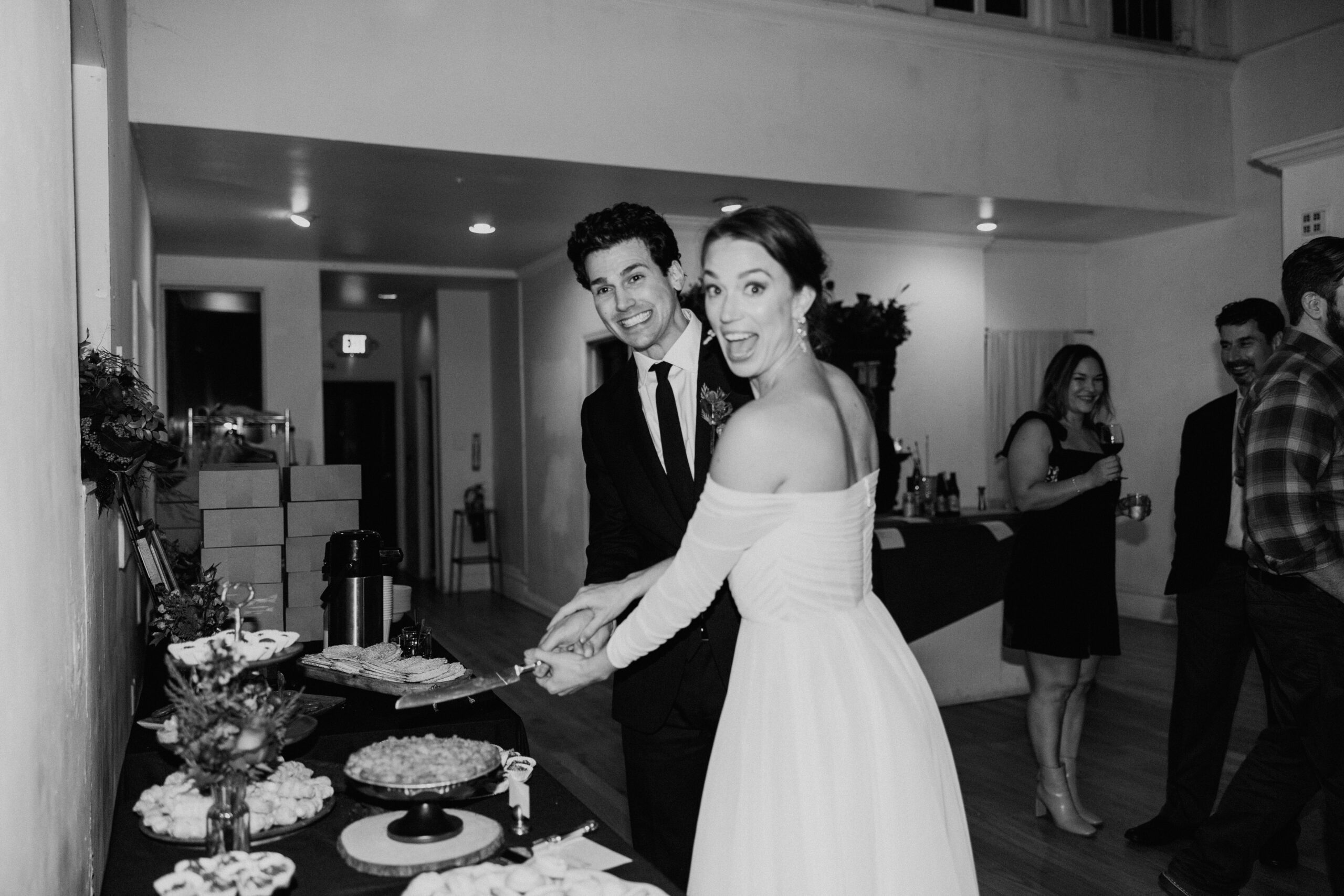A black and white photo of a bride and groom cutting the cake.