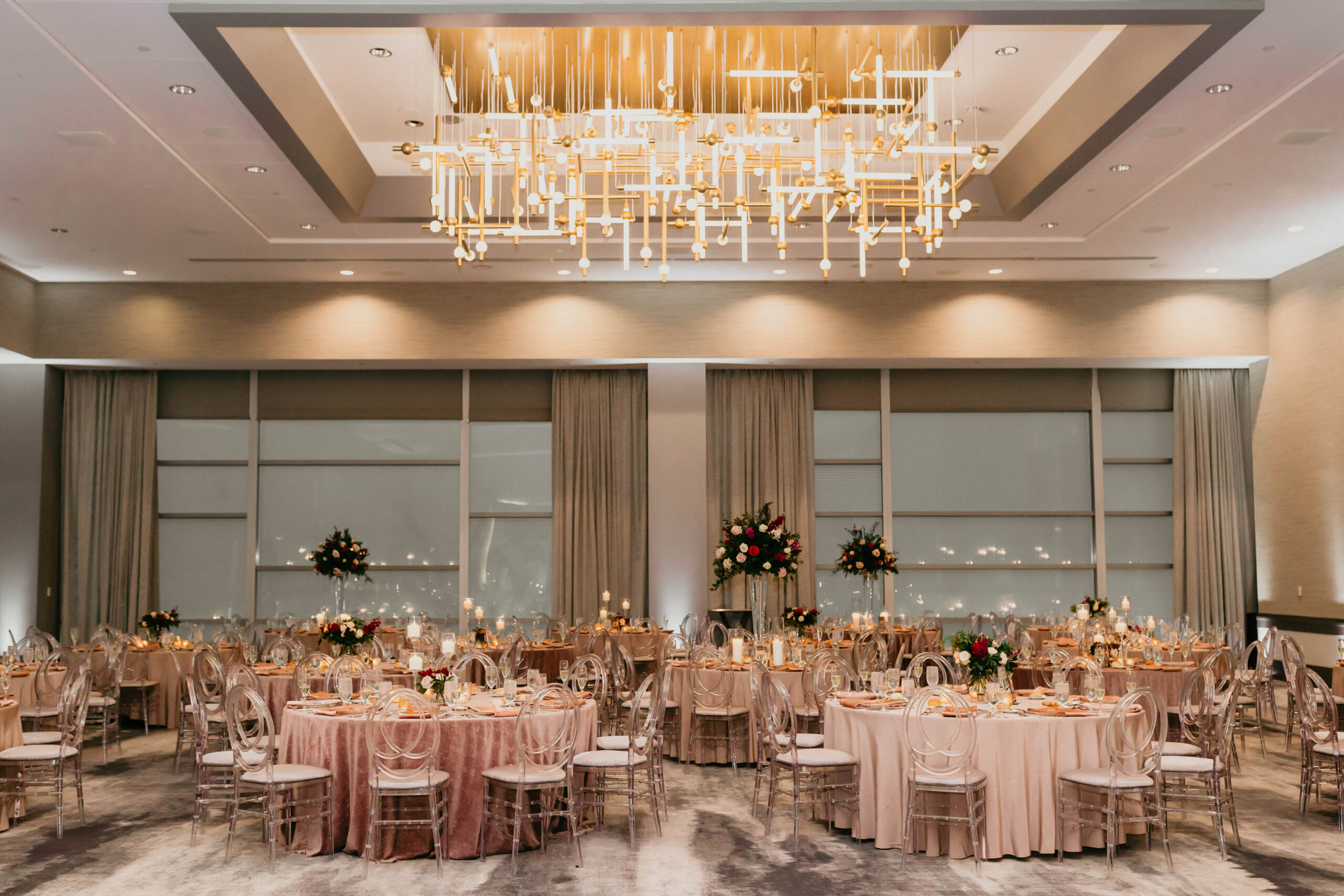 A photo of tables and chairs set up for a wedding reception. A unique chandelier lights the room from above.