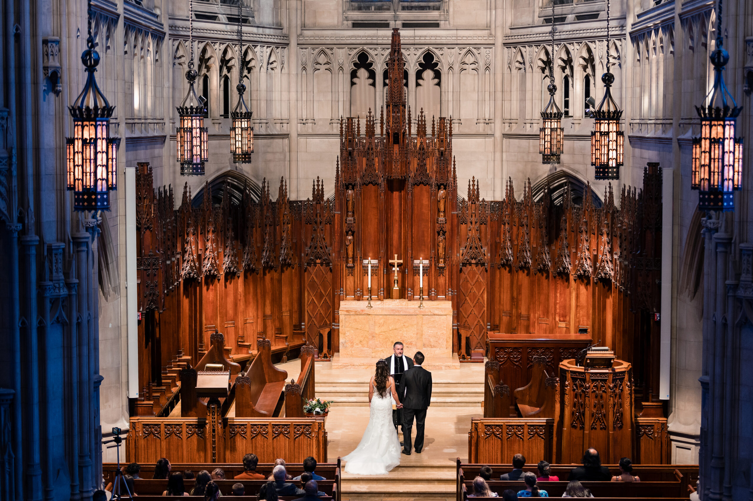 A wide view of a couple getting married at the Heinz Memorial Chapel in front of stunning architecture.