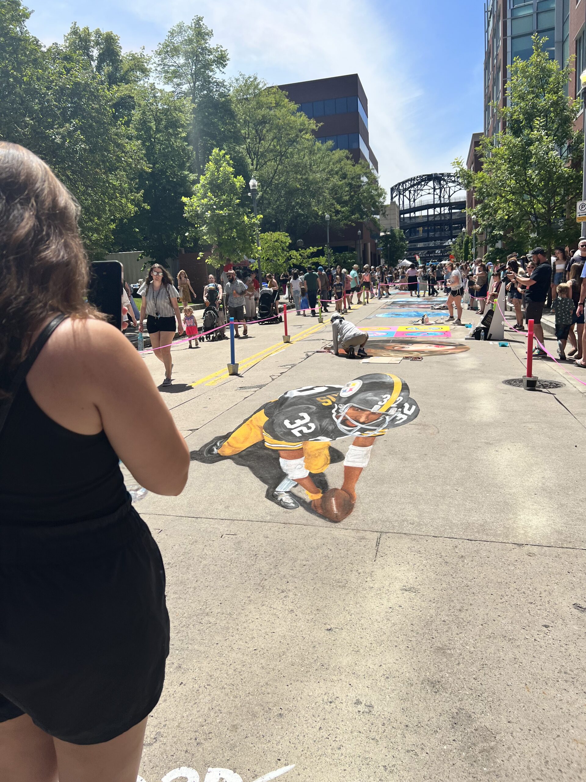 A photo of someone taking a picture of chalk art of Franco Harris in his Steelers uniform.