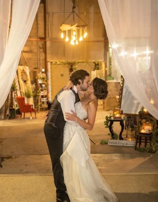 A bride and groom kissing at an entryway at Kinsey Events. Unique furniture and decor are behind them.