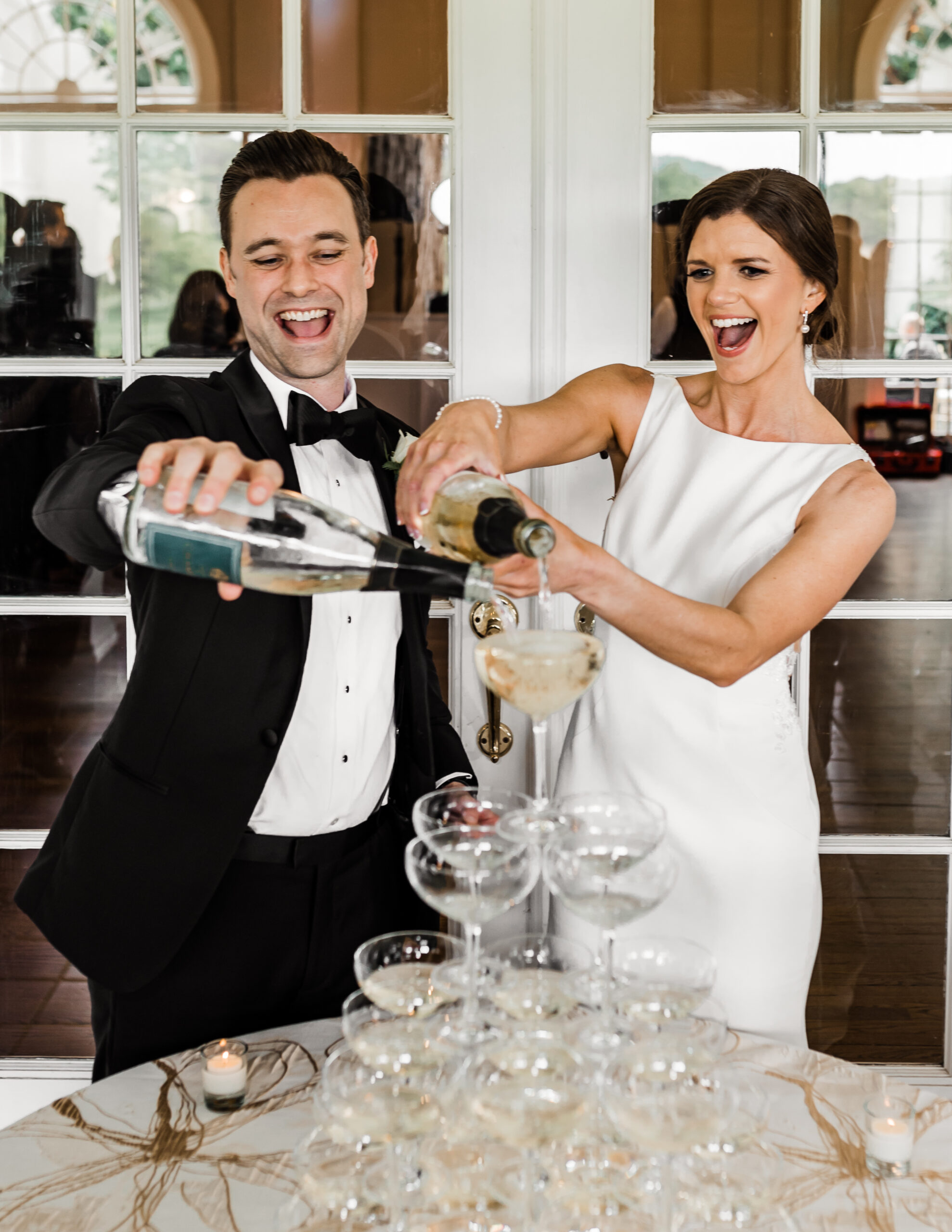 A photo of a bride and groom pouring champagne or wine over a tower of glasses.