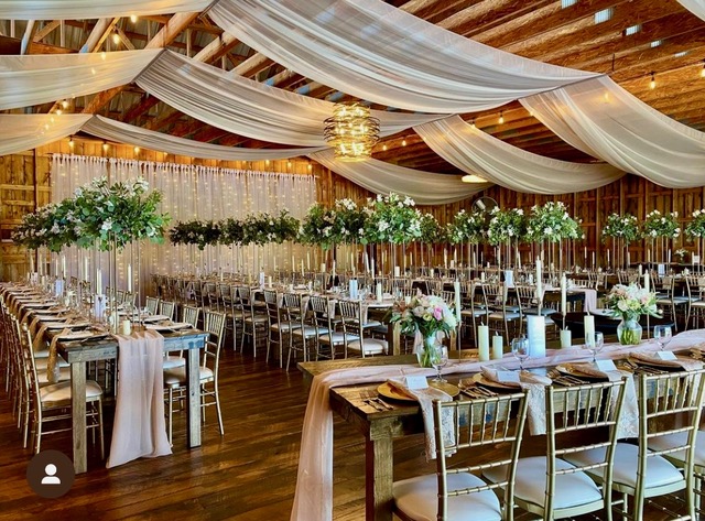 A photo of drapery, florals, and many tables and chairs set up at Pinerock Farm for a wedding reception.