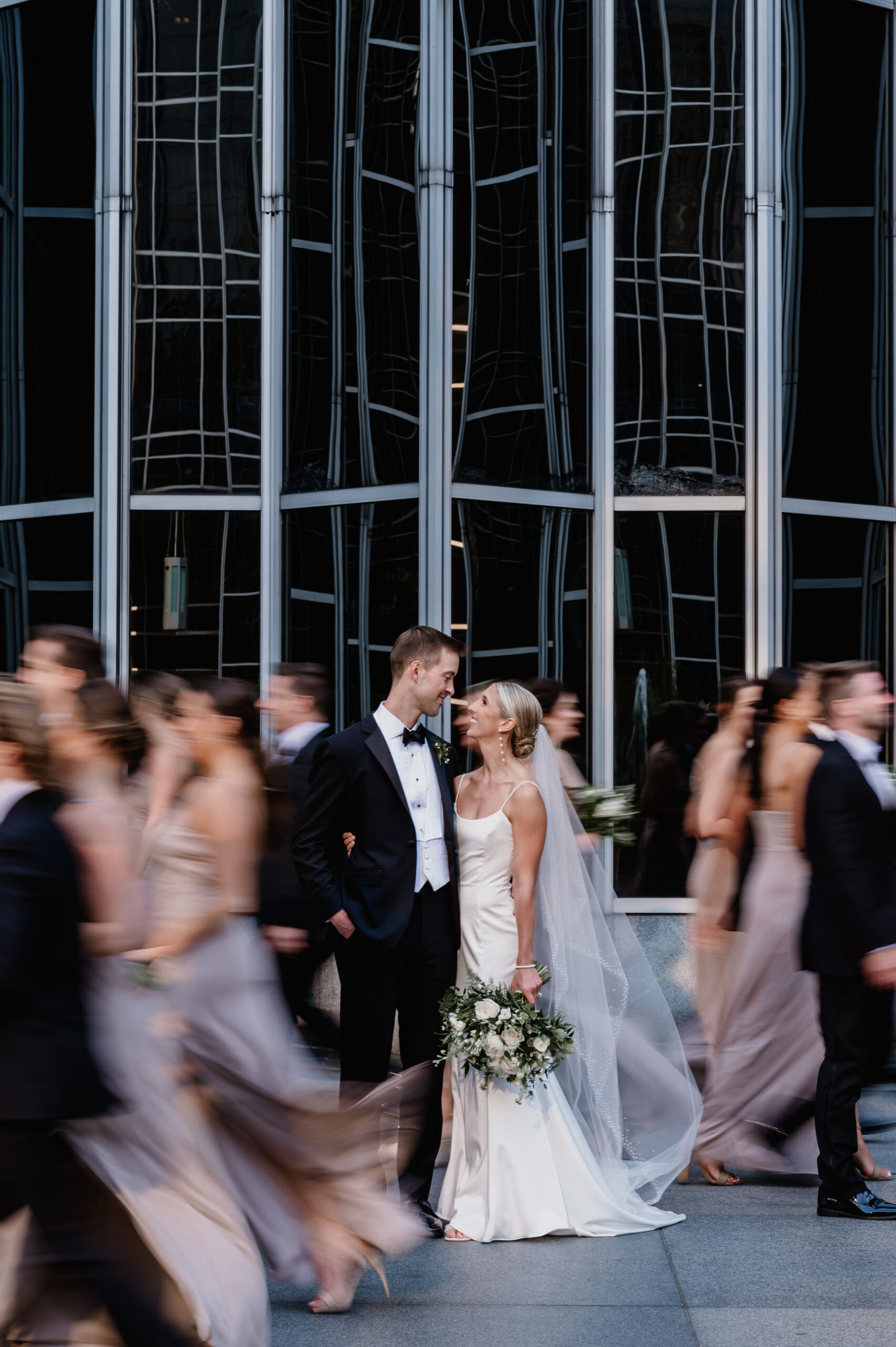 A photo of a bride and groom looking at each other at PPG Plaza. Their wedding party has motion blur surrounding them.