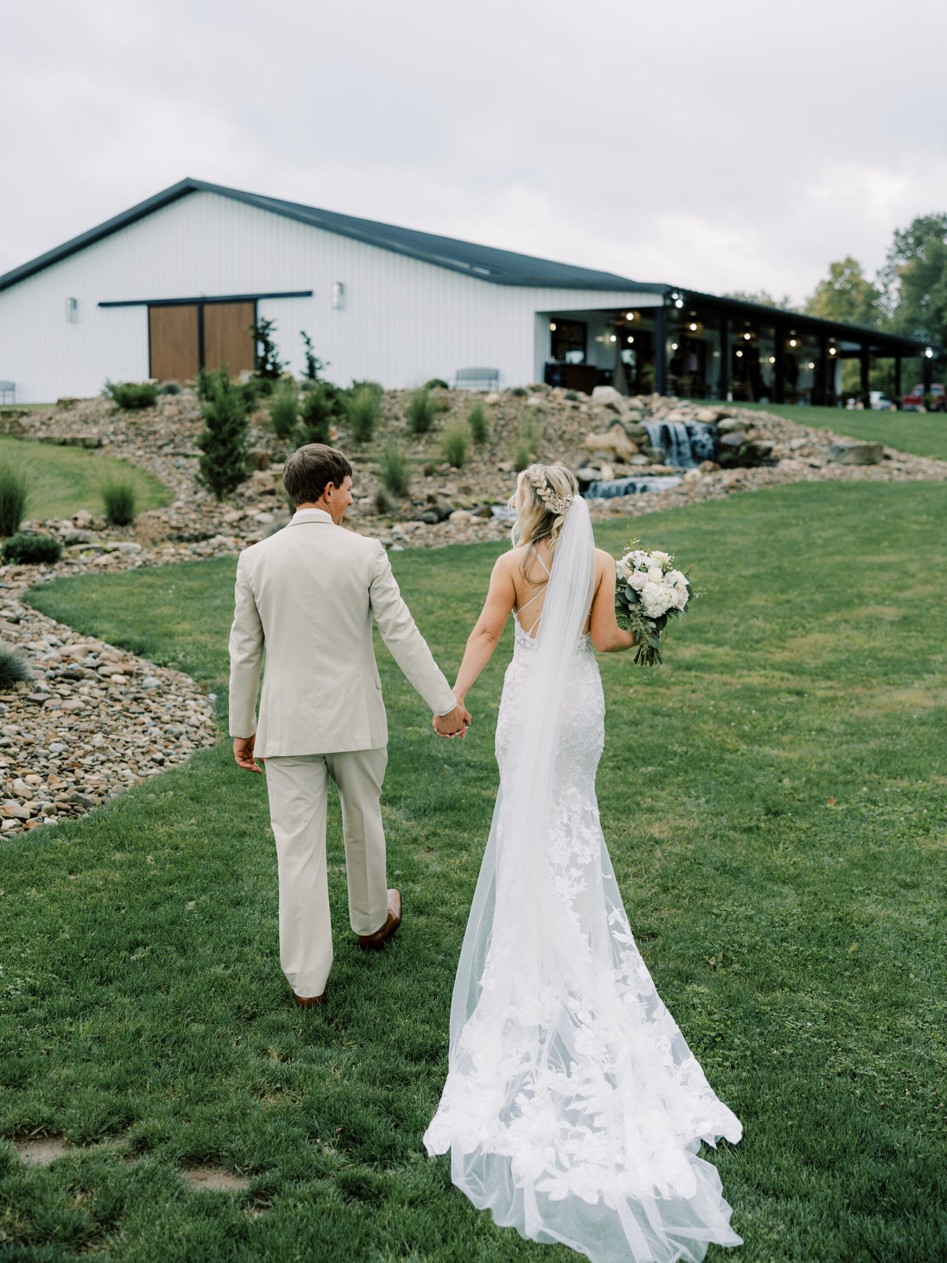A photo of a bride and groom holding hands walking up towards the Harper Event Venue.