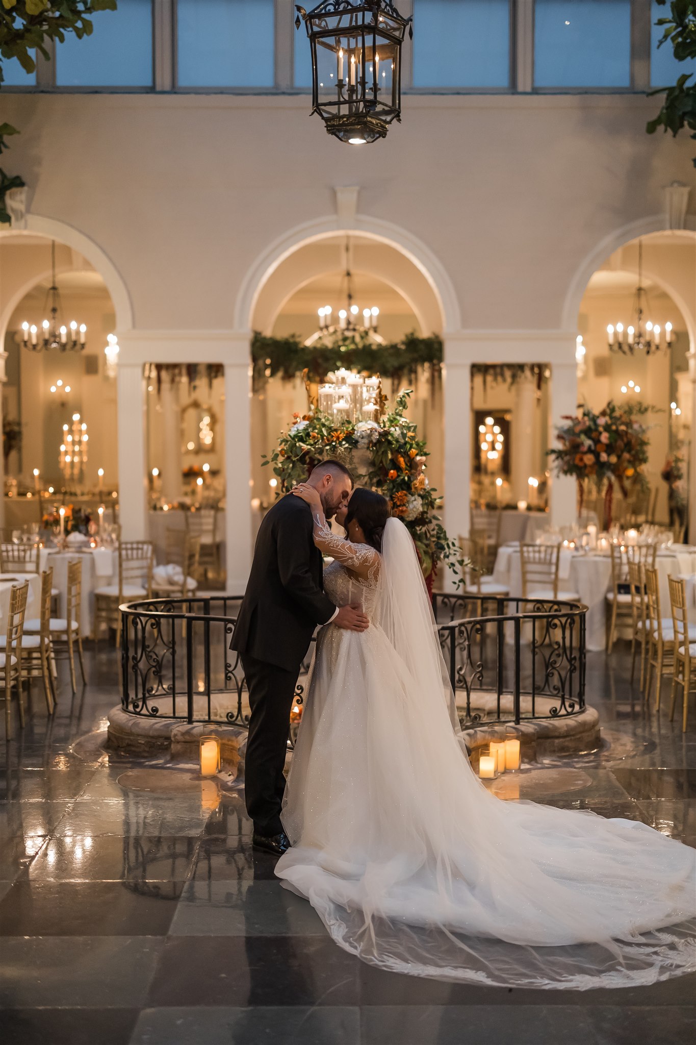 A photo of a bride and groom kissing in a beautifully lit reception area at a wedding.