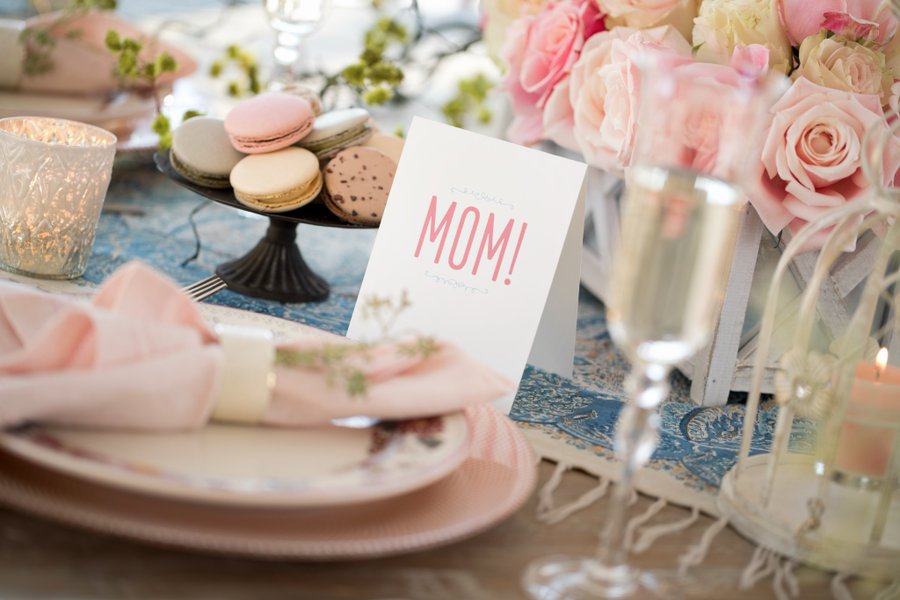 A photo of a table set with light pink flowers and accents with a card that says "MOM!" in the center.