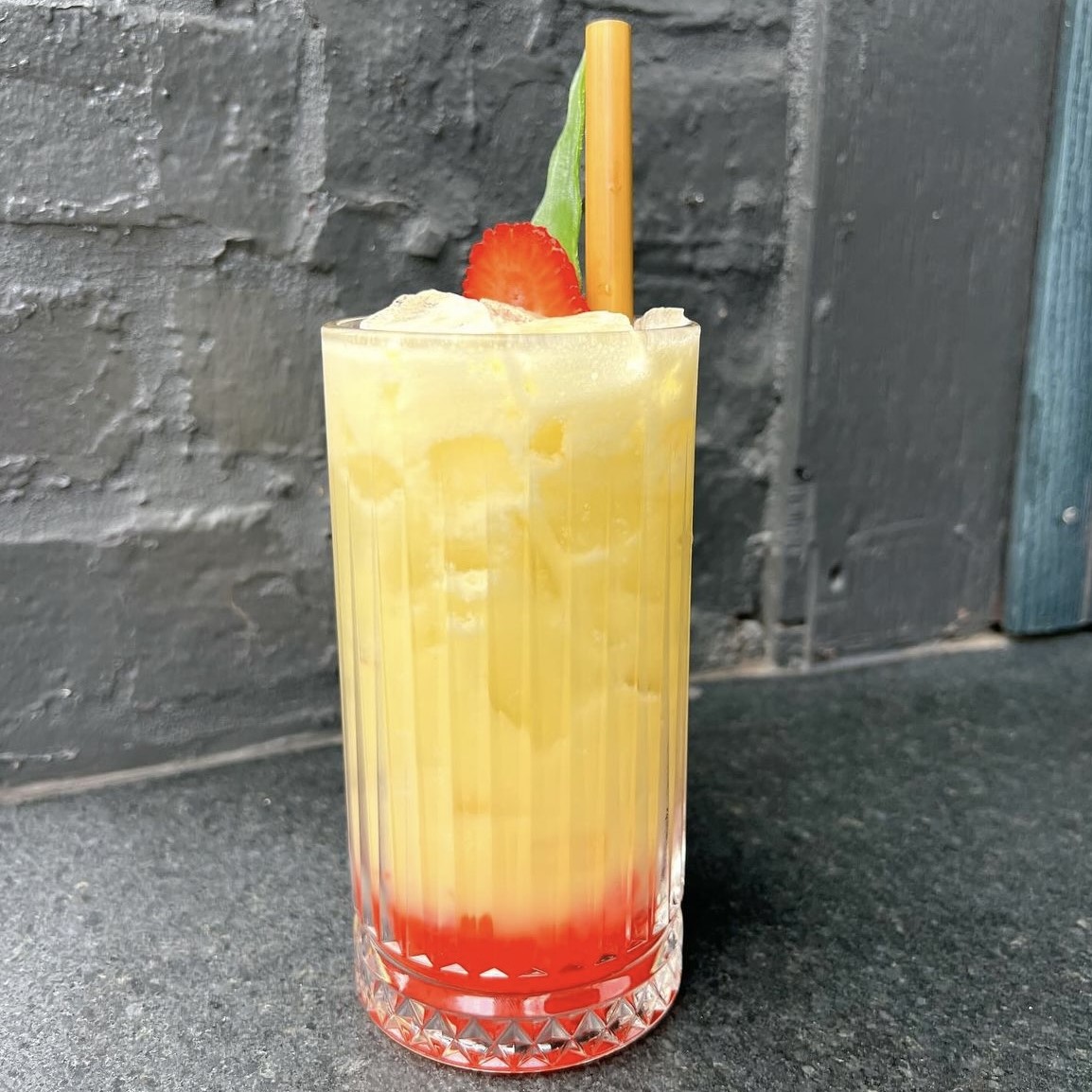 A photo of the Parlor Smoothie Club drink with a strawberry slice on top and a straw.