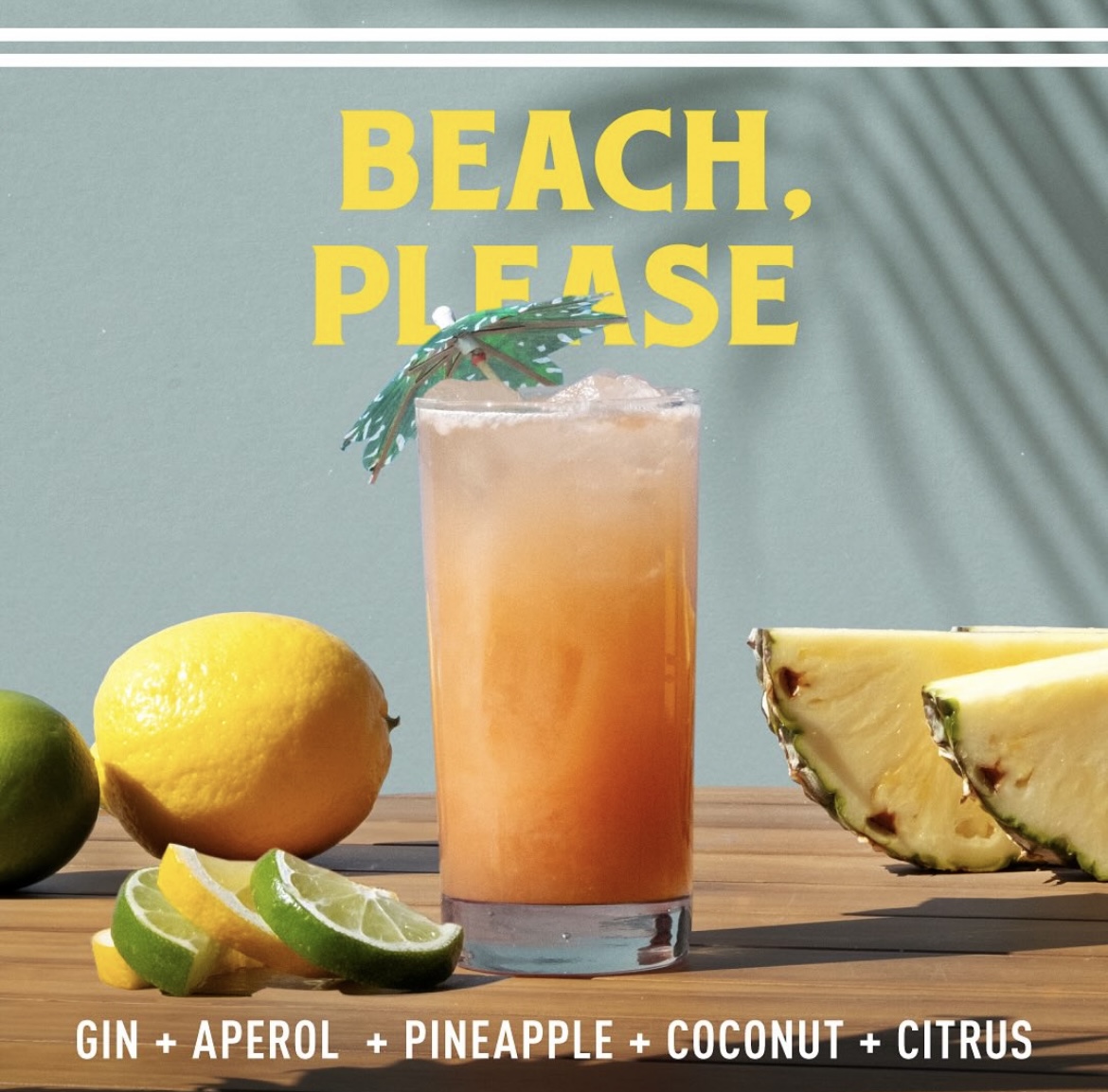 A photo of the Beach, Please cocktail in a tall glass with a paper umbrella in it. The glass is surrounded by pineapple, lemon, and lime.