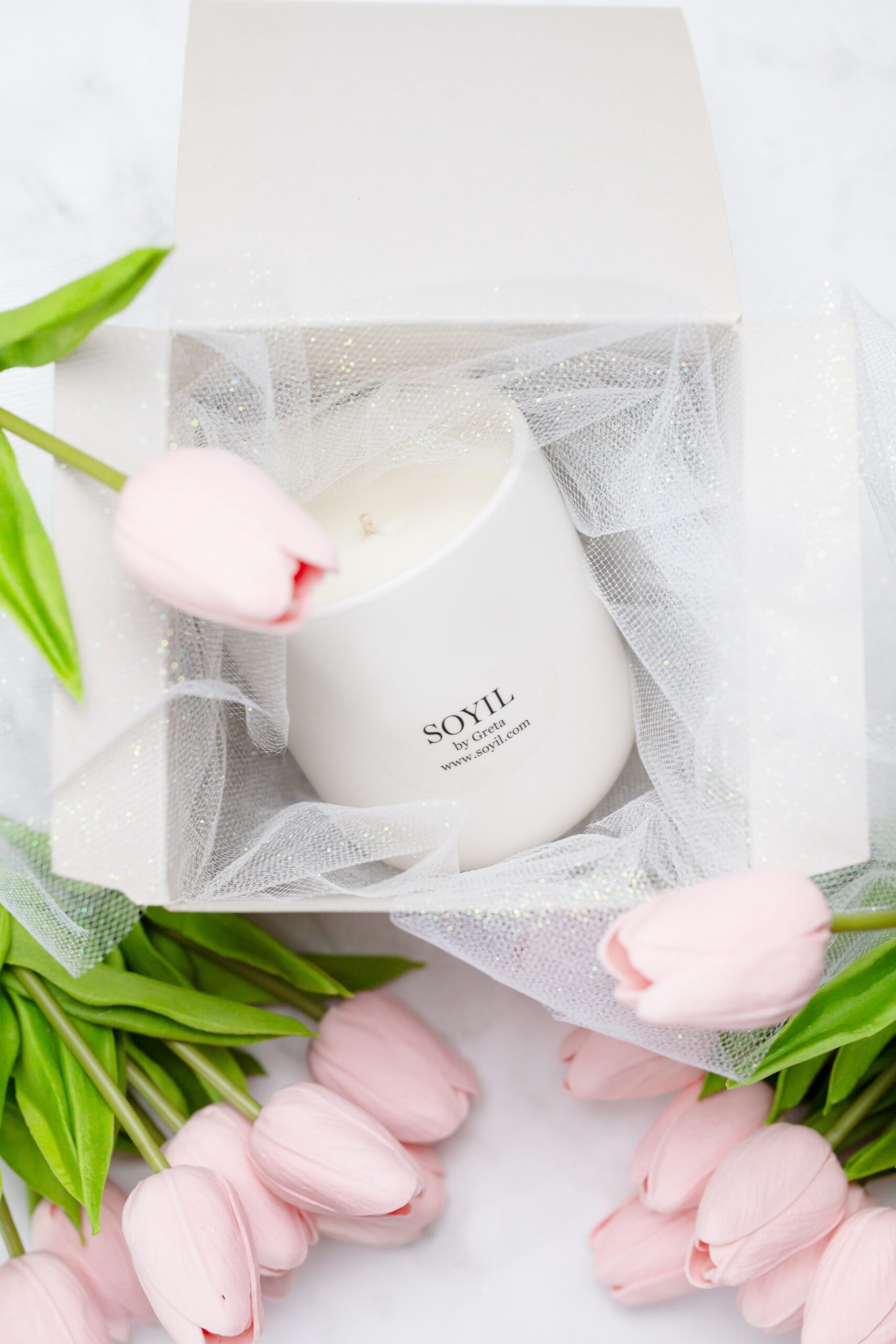 A photo of a Soyil candle in a box with tulle and flowers surrounding it.