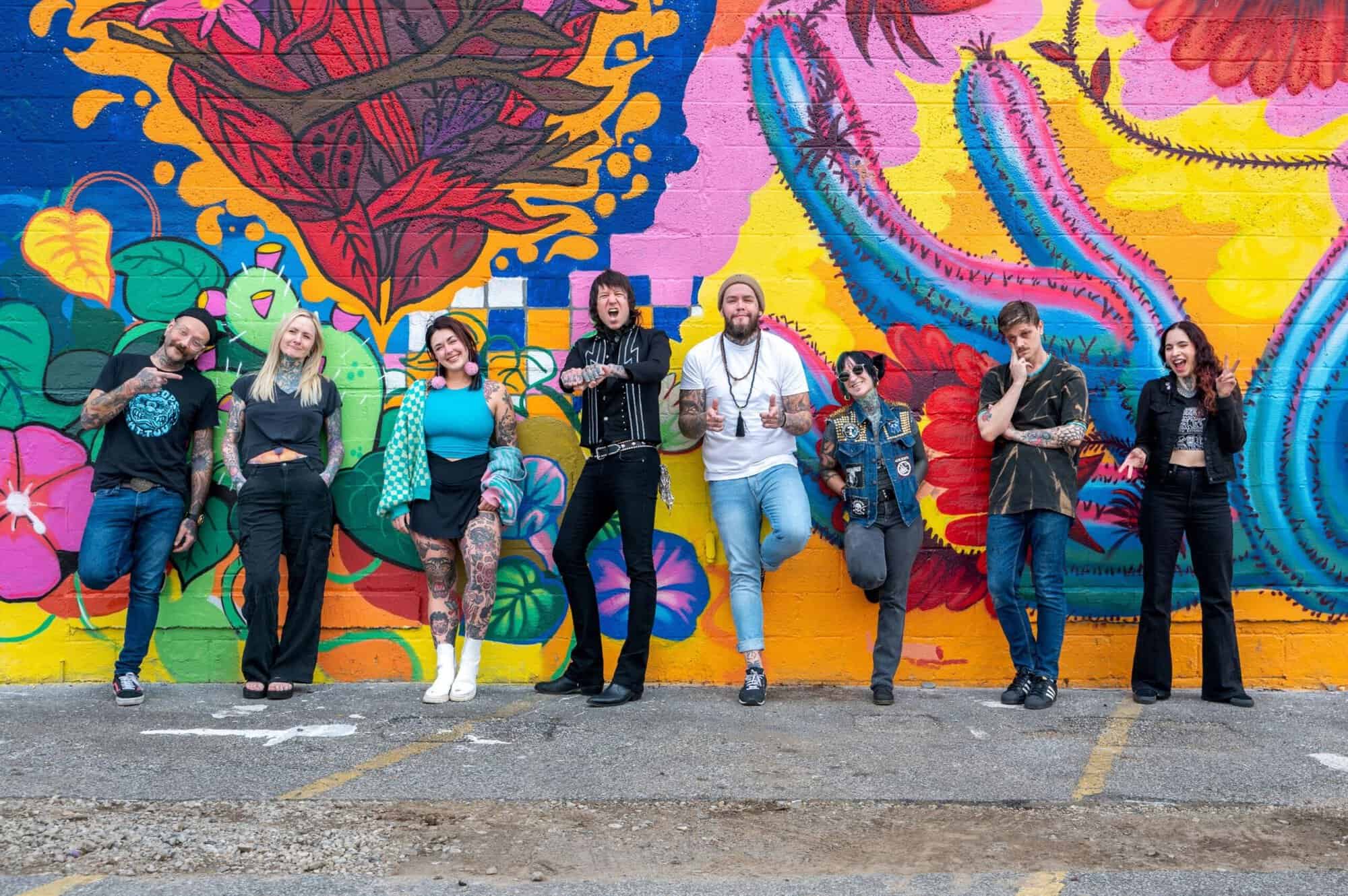 A photo of eight Ink for Impact tattoo artists posing in front of a colorful mural.
