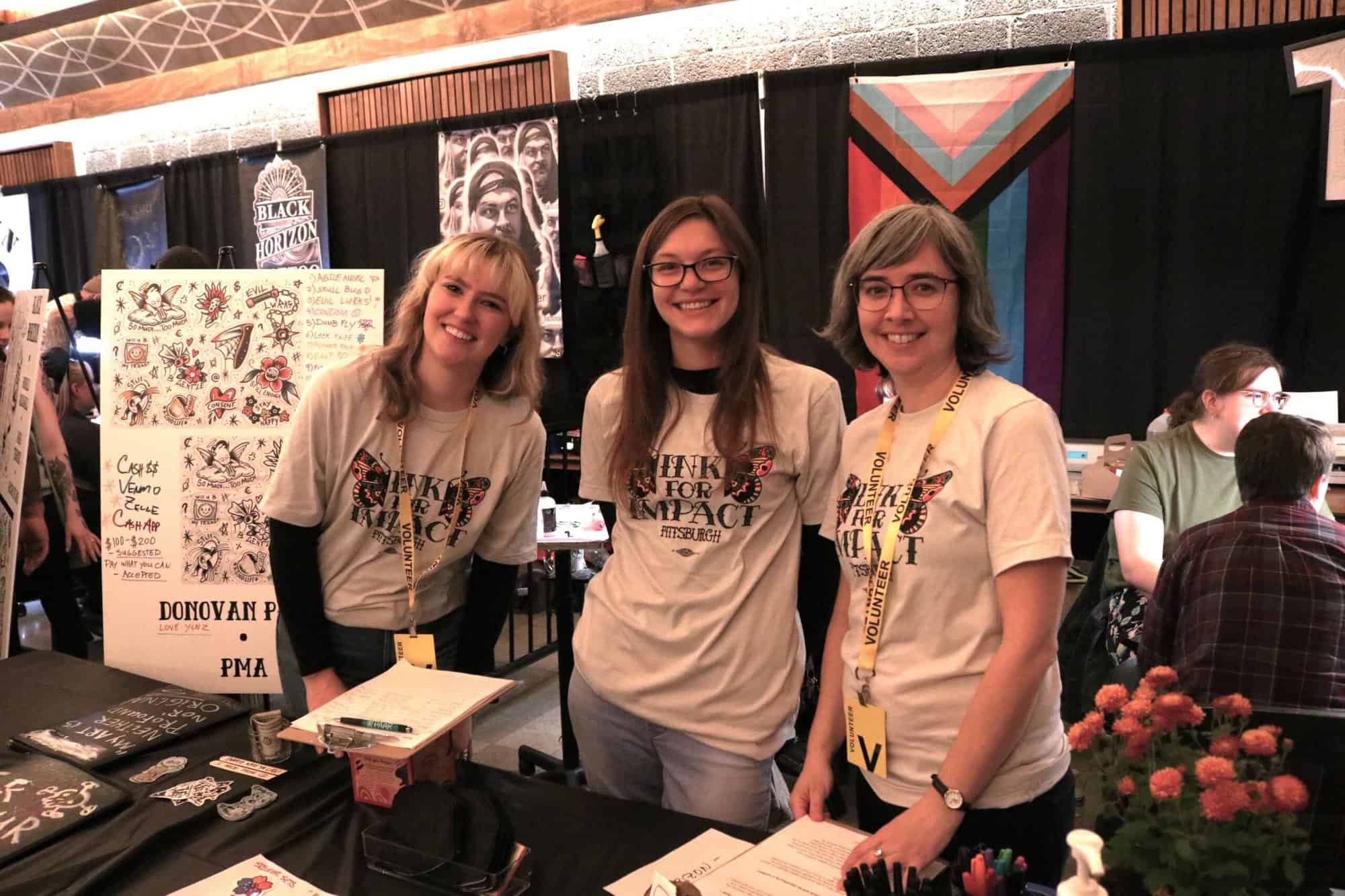 A photo of three people wearing Ink for Impact shirts at the 2023 event.