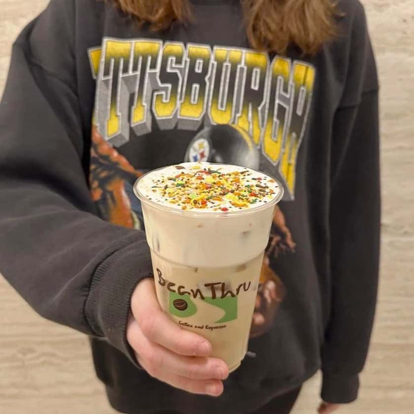 A photo of a person in a Pittsburgh Steelers sweatshirt holding a BeanThru iced coffee with cold foam and sprinkles.