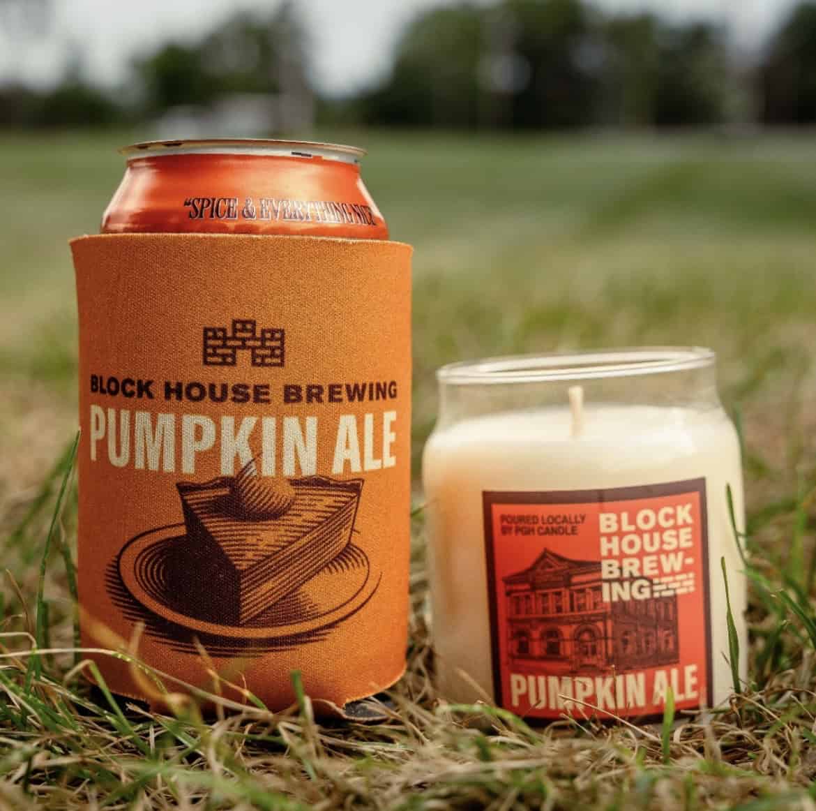 A photo of a Block House Brewing Pumpkin Ale in a koozie, with a candle with the same flavor/scent next to it.