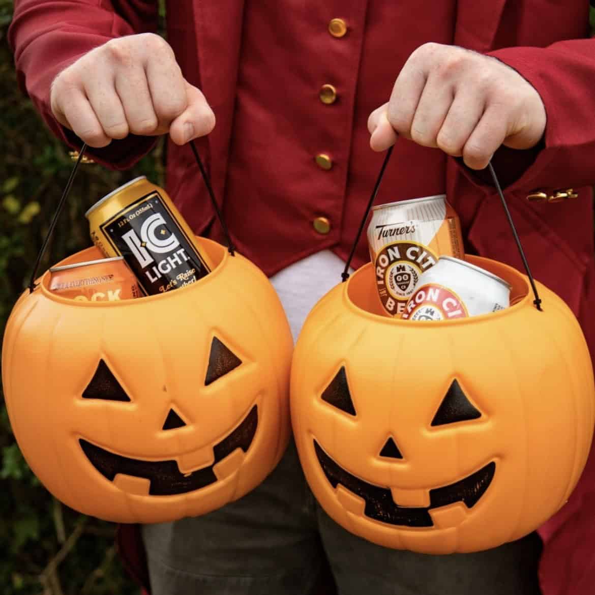 A photo of a person holding two pumpkin jack-o-lantern baskets full of Iron City Beer and IC Light cans.